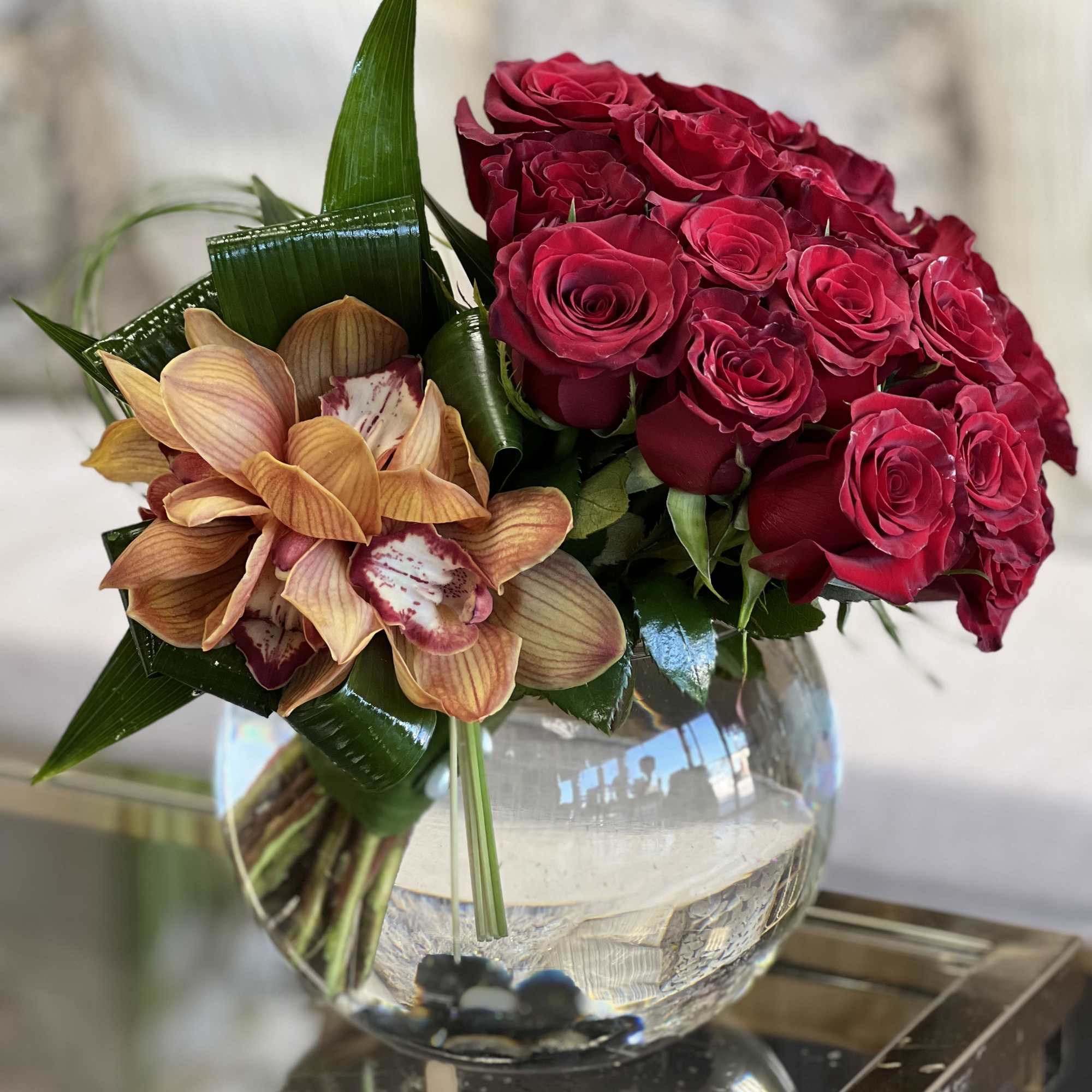 A tight cluster of red Roses, accented with Cymbidium Orchids and set