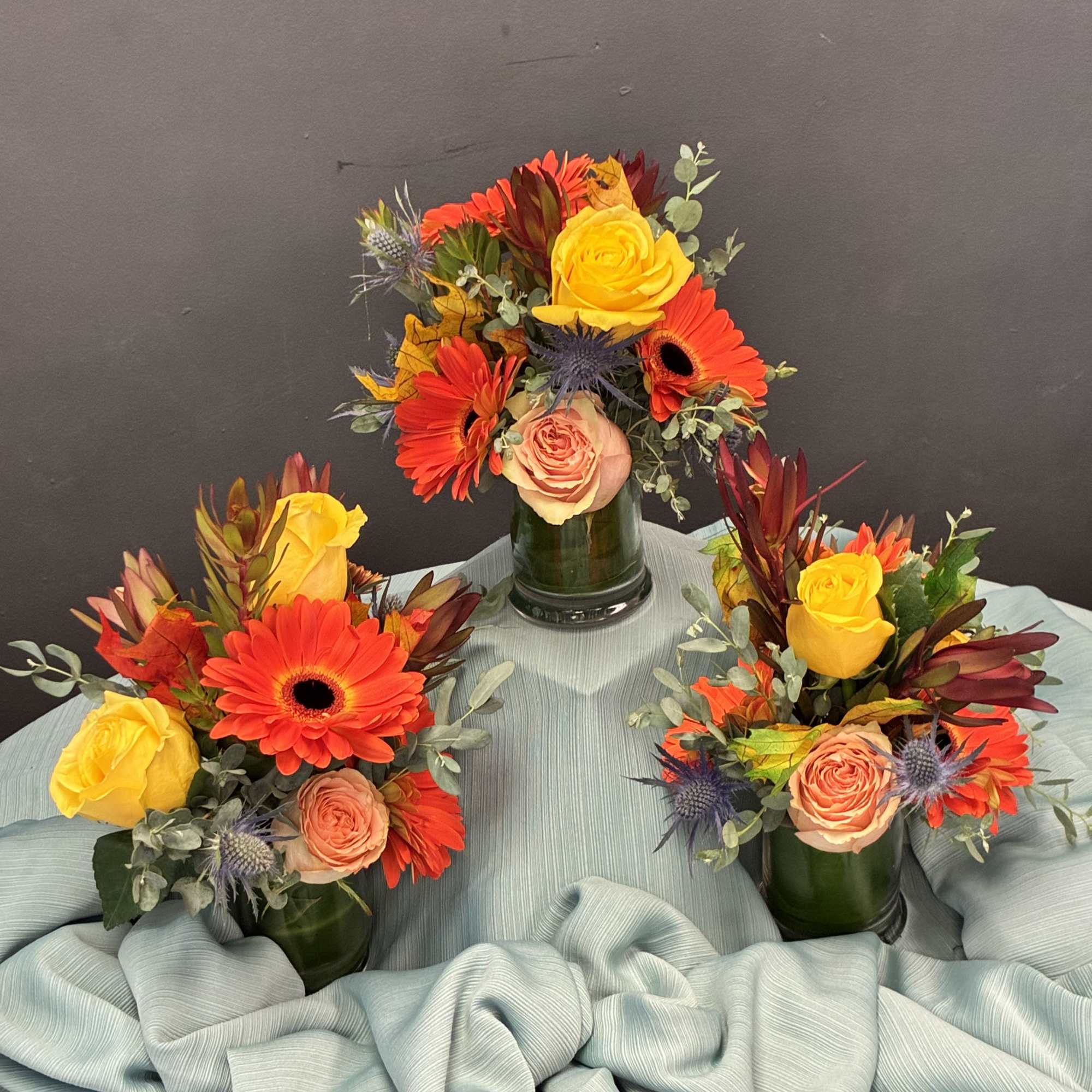 petite arrangements glow with sunset-inspired warmth and texture. Each green glass vase