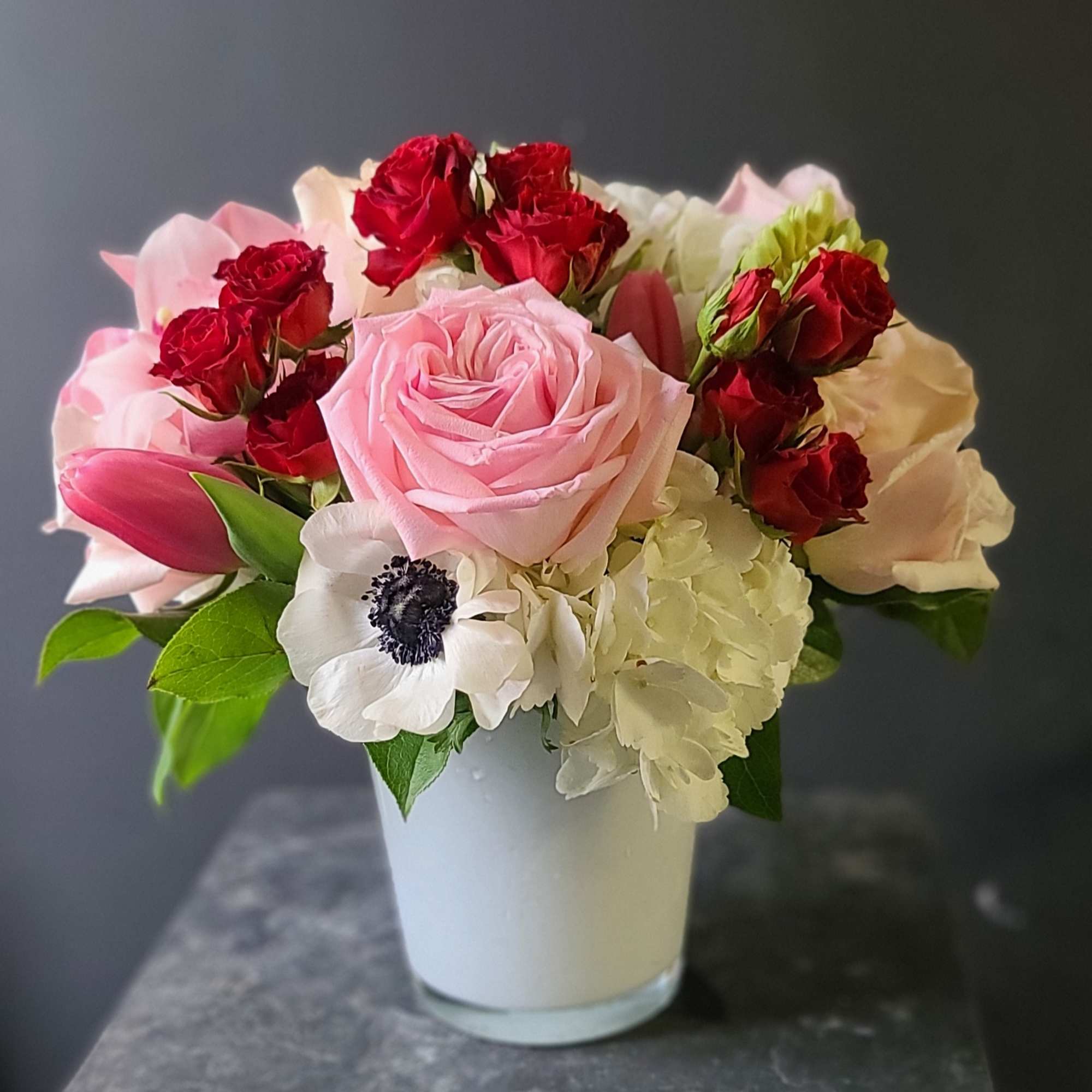 A sweet arrangement of spray roses, roses, hydrangea, tulips, and anemones. 