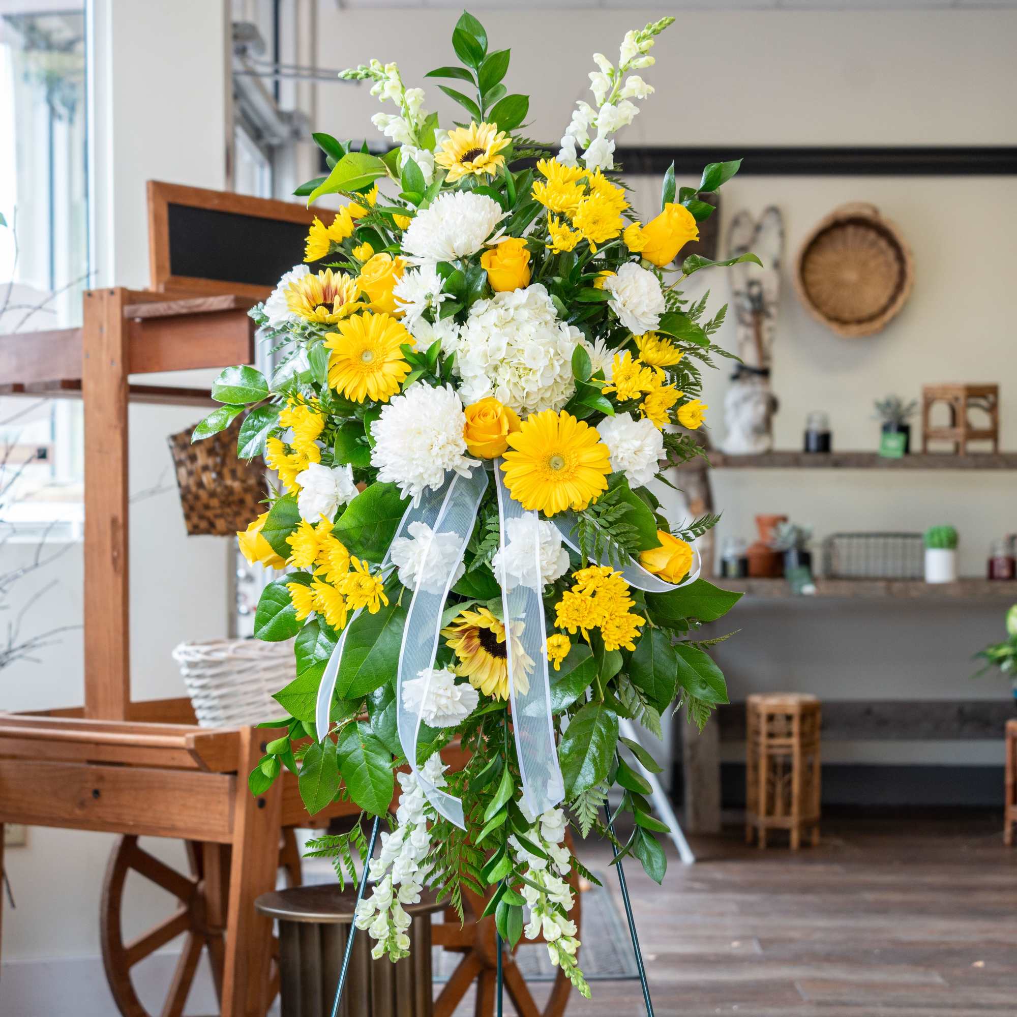 And easel arrangement featuring yellow gerber daisy's, yellow roses, sunflowers, yellow cremon