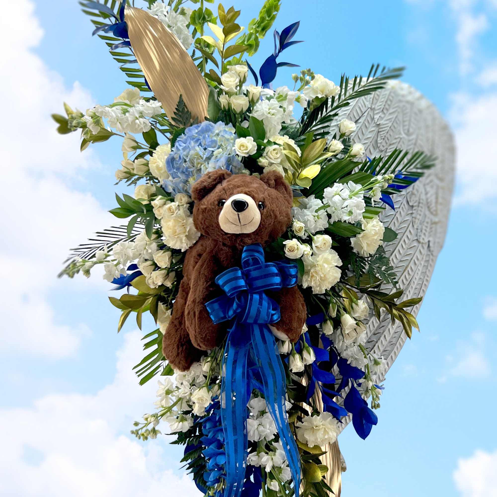 A metal angel wing spray adorned with a keepsake plush teddy bear.