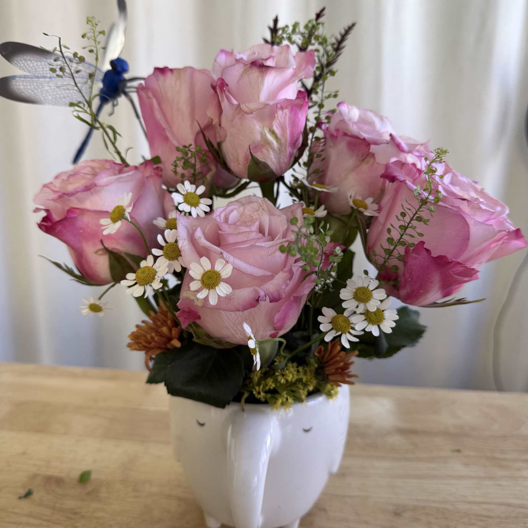 A sweet and charming arrangement featuring soft pink roses, daisies, and fresh