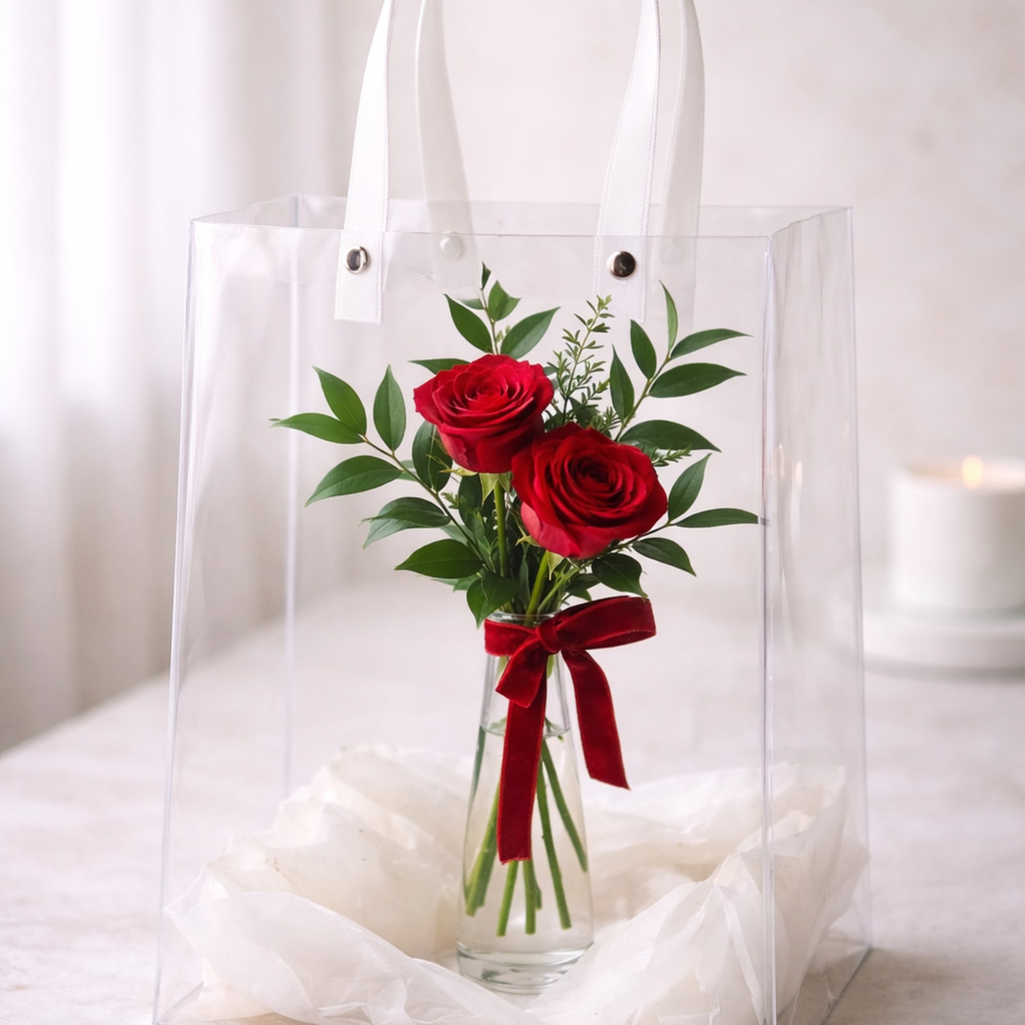 Two passionate red roses rest inside a slender glass bud vase, embraced