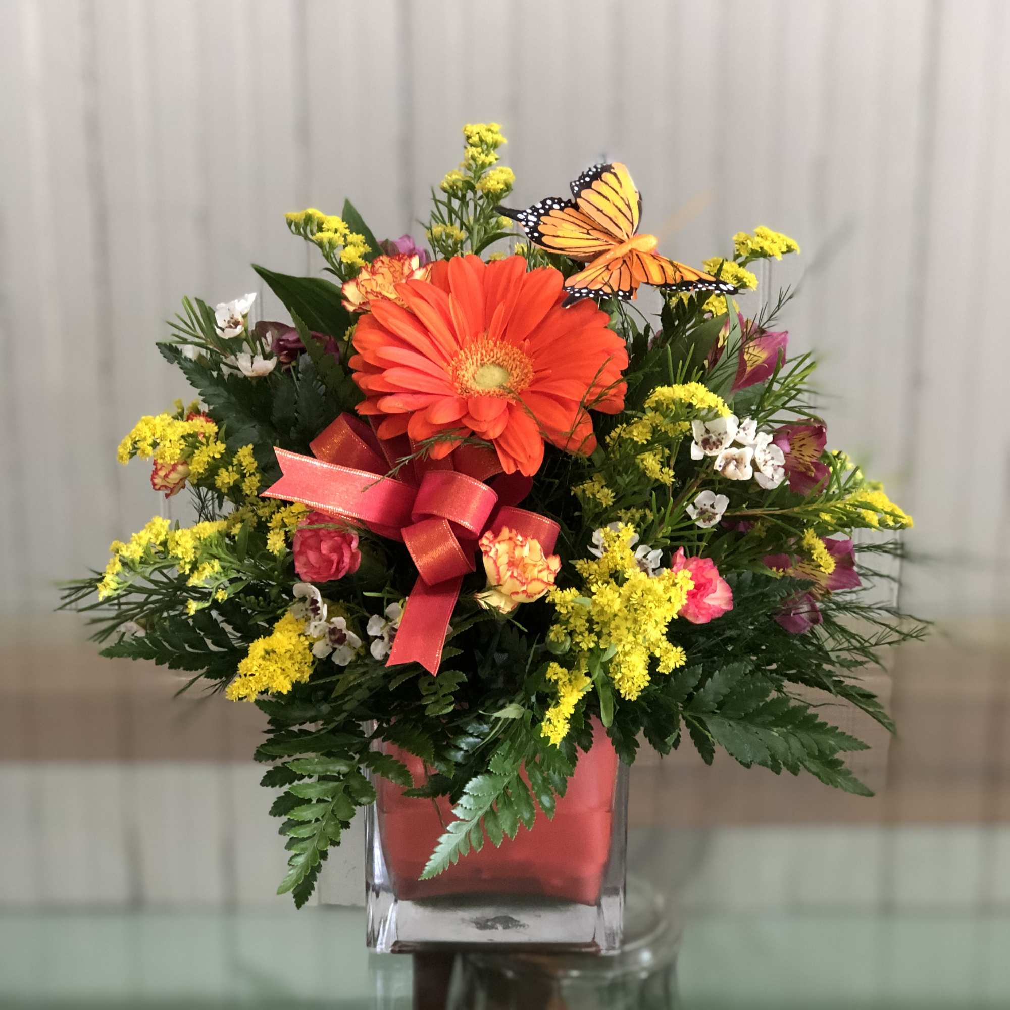 A cube vase filled with gerbera daisies, alstromeria, baby's breath, wax flower