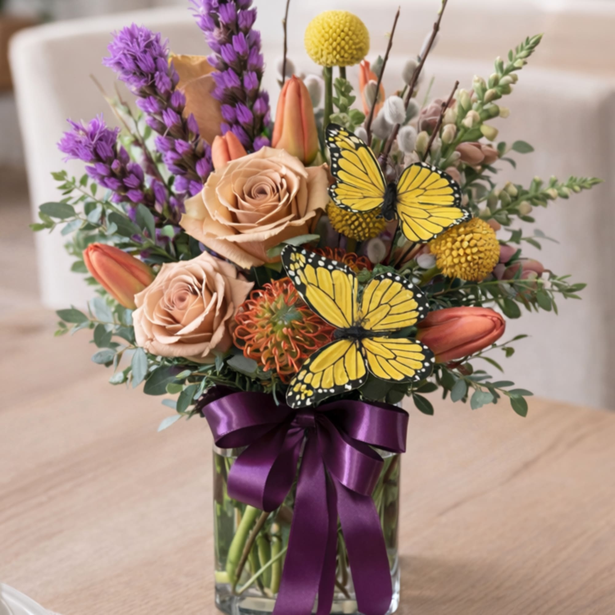 A lush, garden-style flower arrangement featuring roses, tulips, seasonal blooms, and decorative