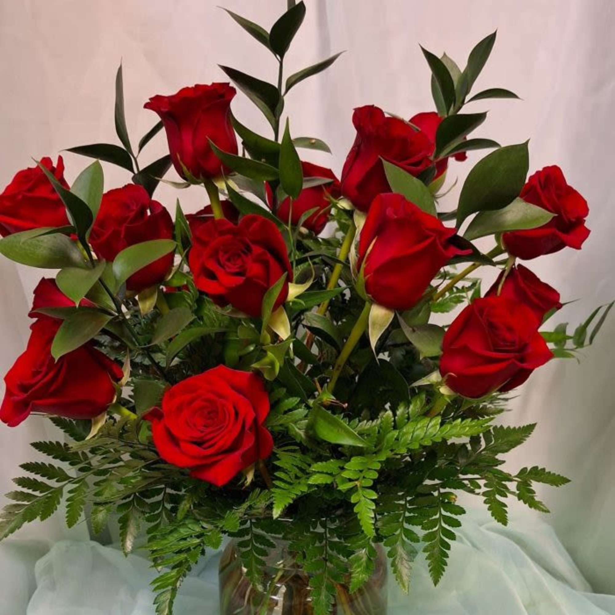 One dozen red roses and assorted greenery, arranged in a clear cinch