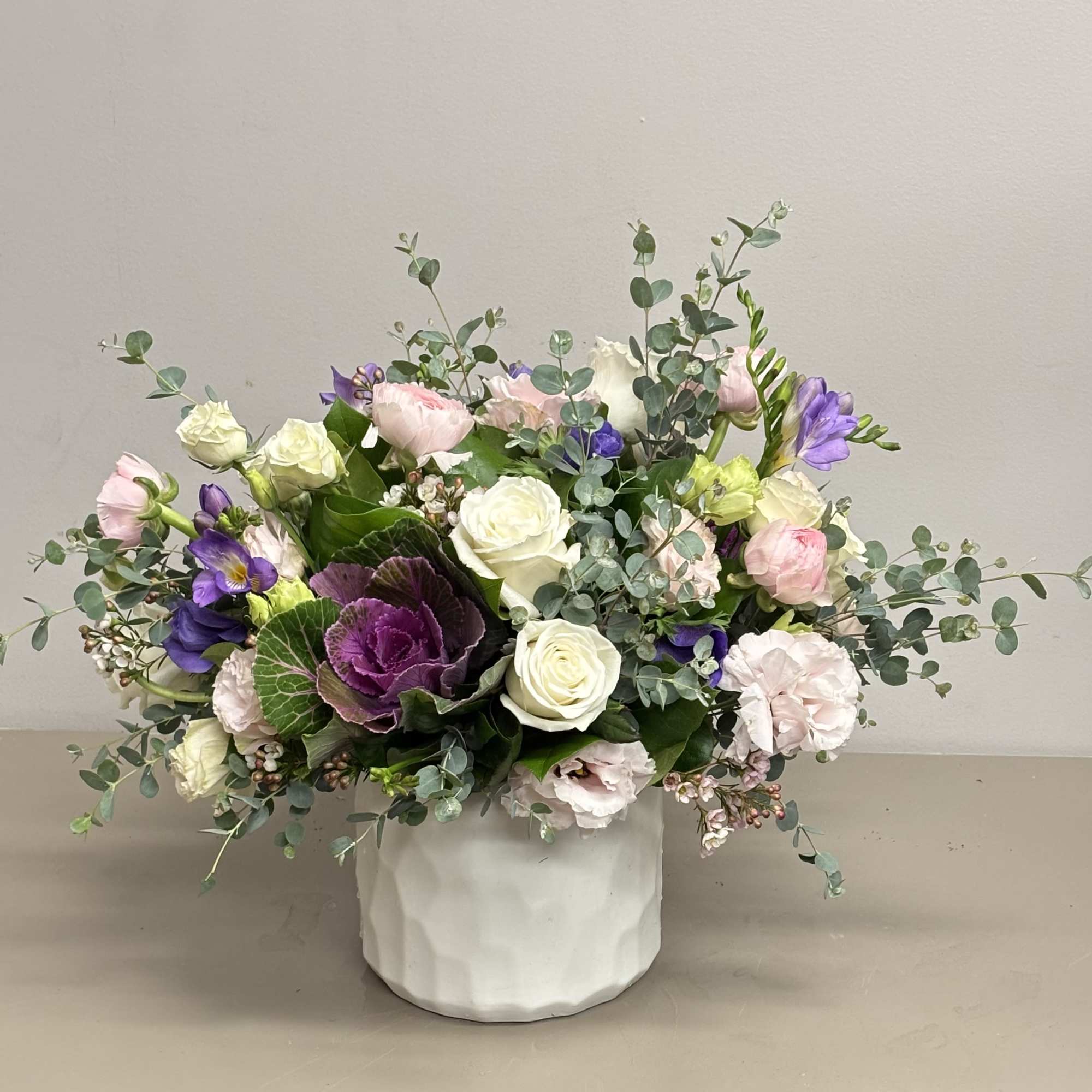 A garden style arrangement beautifully designed with Roses, Ranunculus, Lisianthus, Kale and