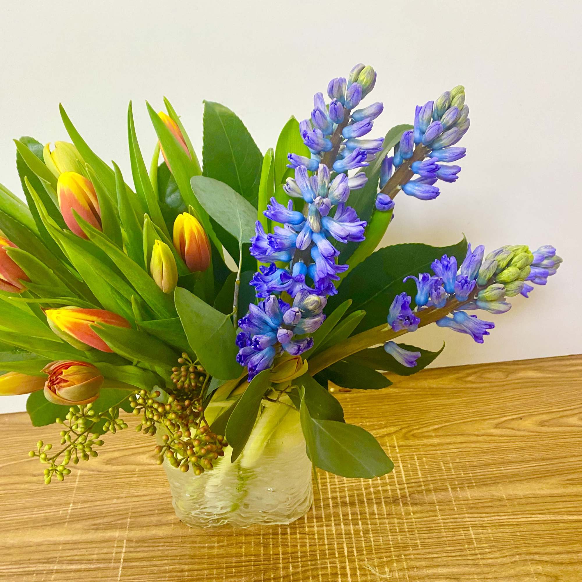 Orange tulips and blue hyacinths in a glass vase with some greenery
Colors