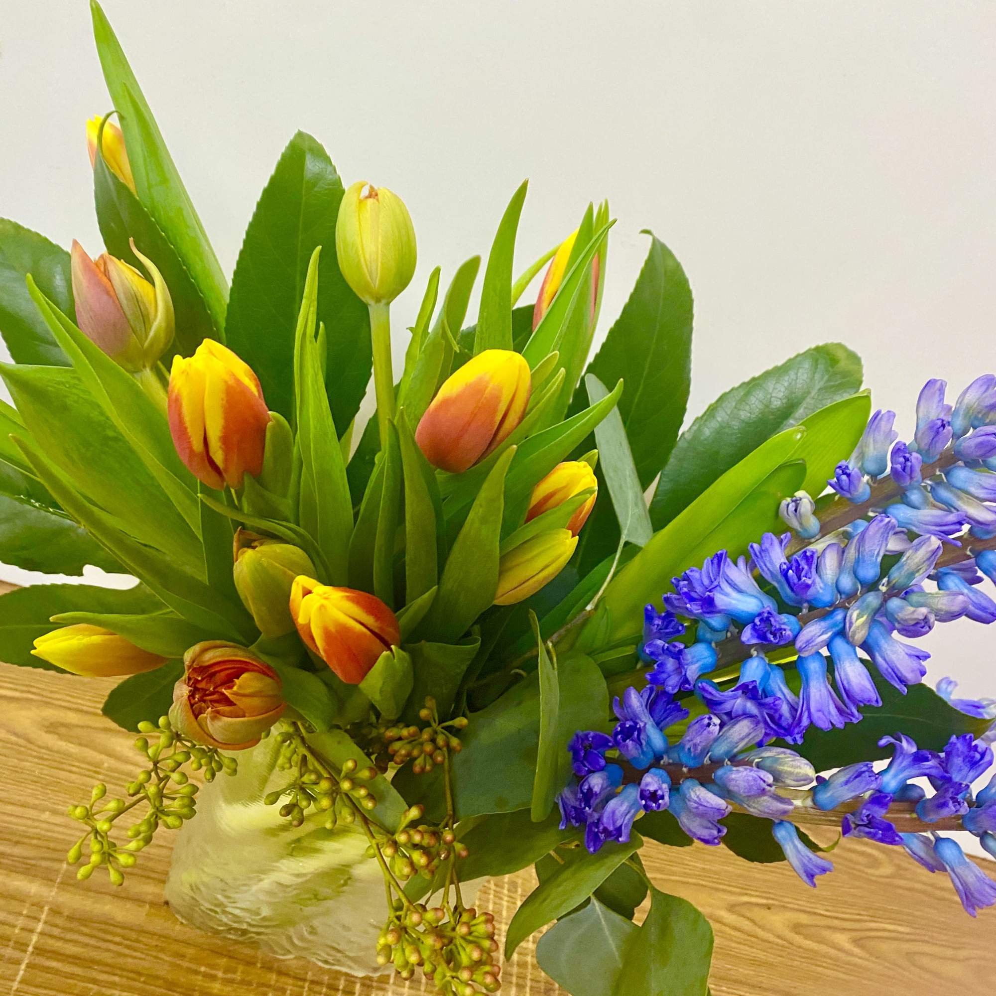 Orange tulips and blue hyacinths in a glass vase with some greenery
Colors