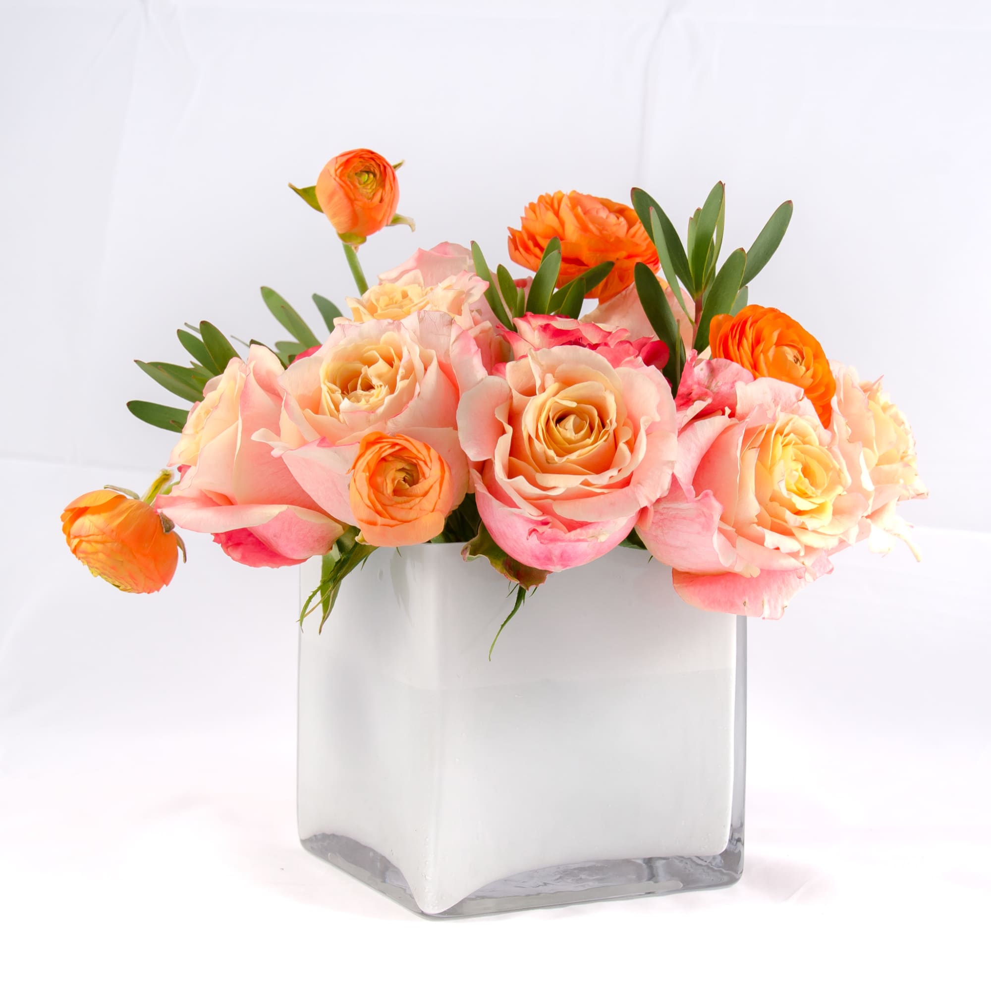 Sweet pastel colors of sherbet roses, orange ranunculus, petite green leaves arranged