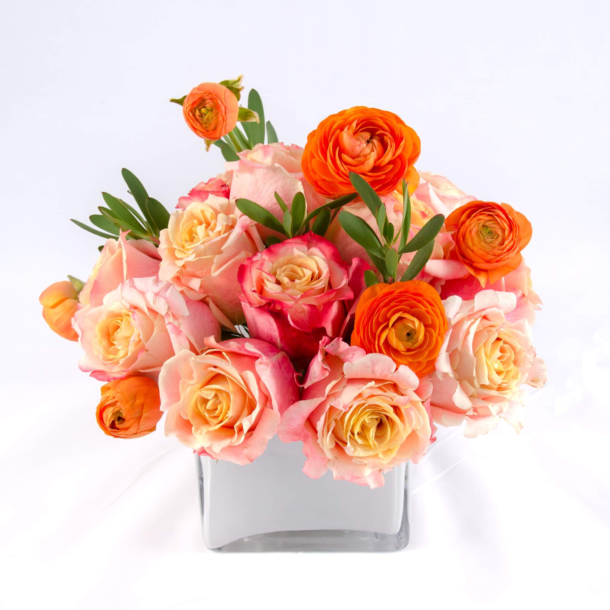 Sweet pastel colors of sherbet roses, orange ranunculus, petite green leaves arranged