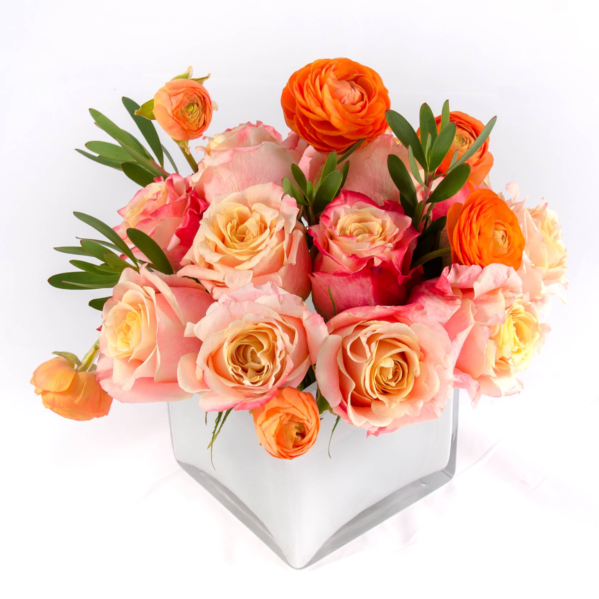 Sweet pastel colors of sherbet roses, orange ranunculus, petite green leaves arranged