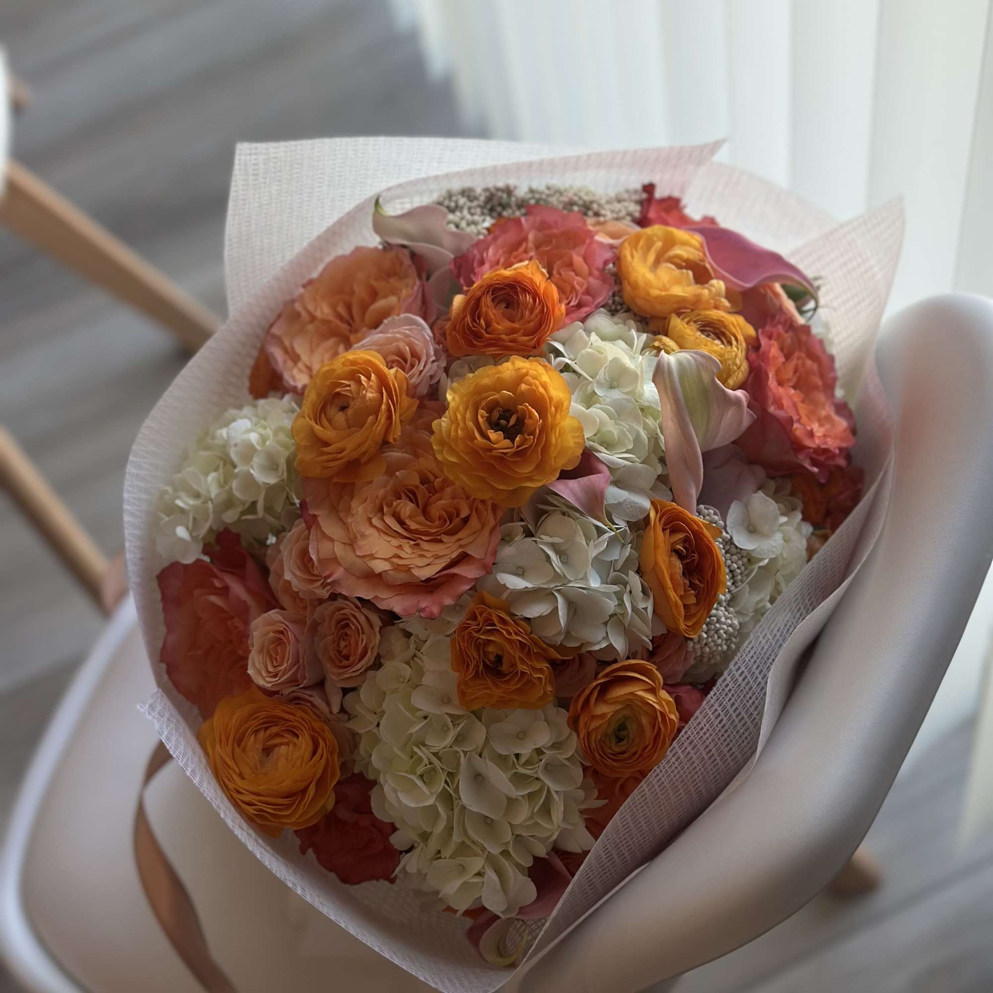 A vibrant blend of fiery ranunculus, peach roses, creamy hydrangeas, and playful
