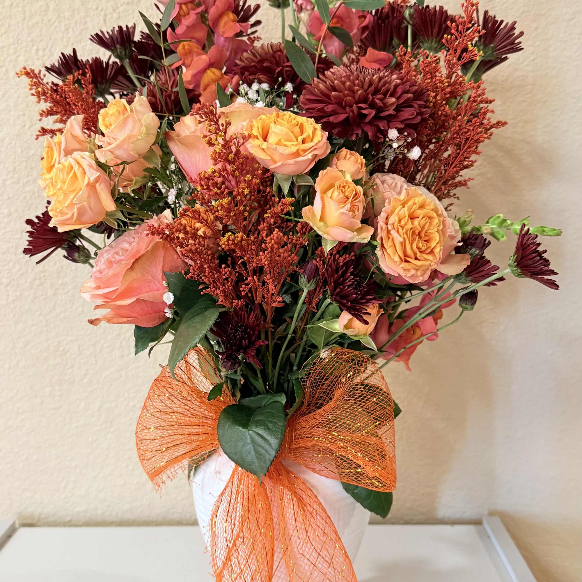 Rich burgundy blooms meet soft peach roses, accented with snapdragons, greenery, and