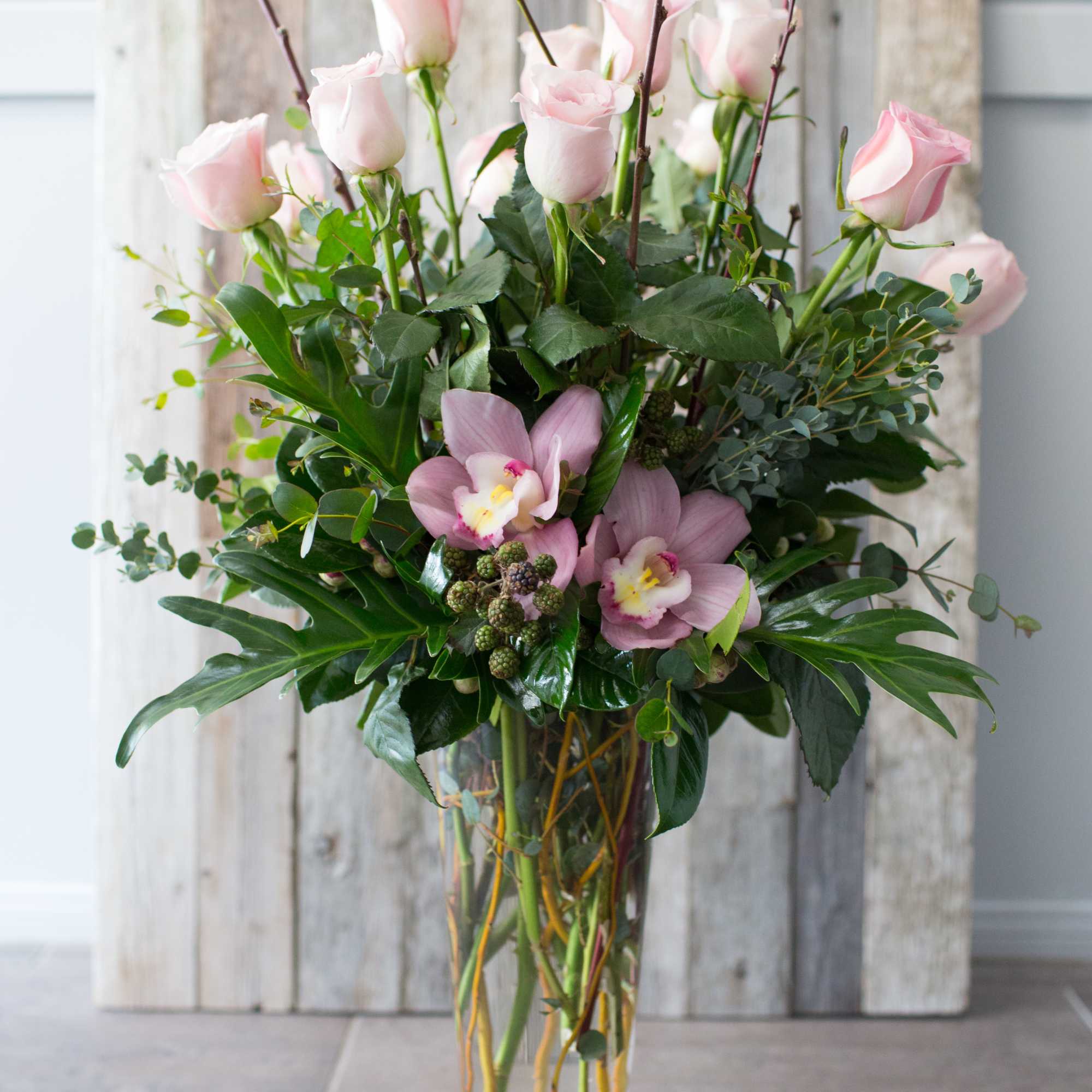 A dozen pink roses adorned with premium greenery and flowering branches