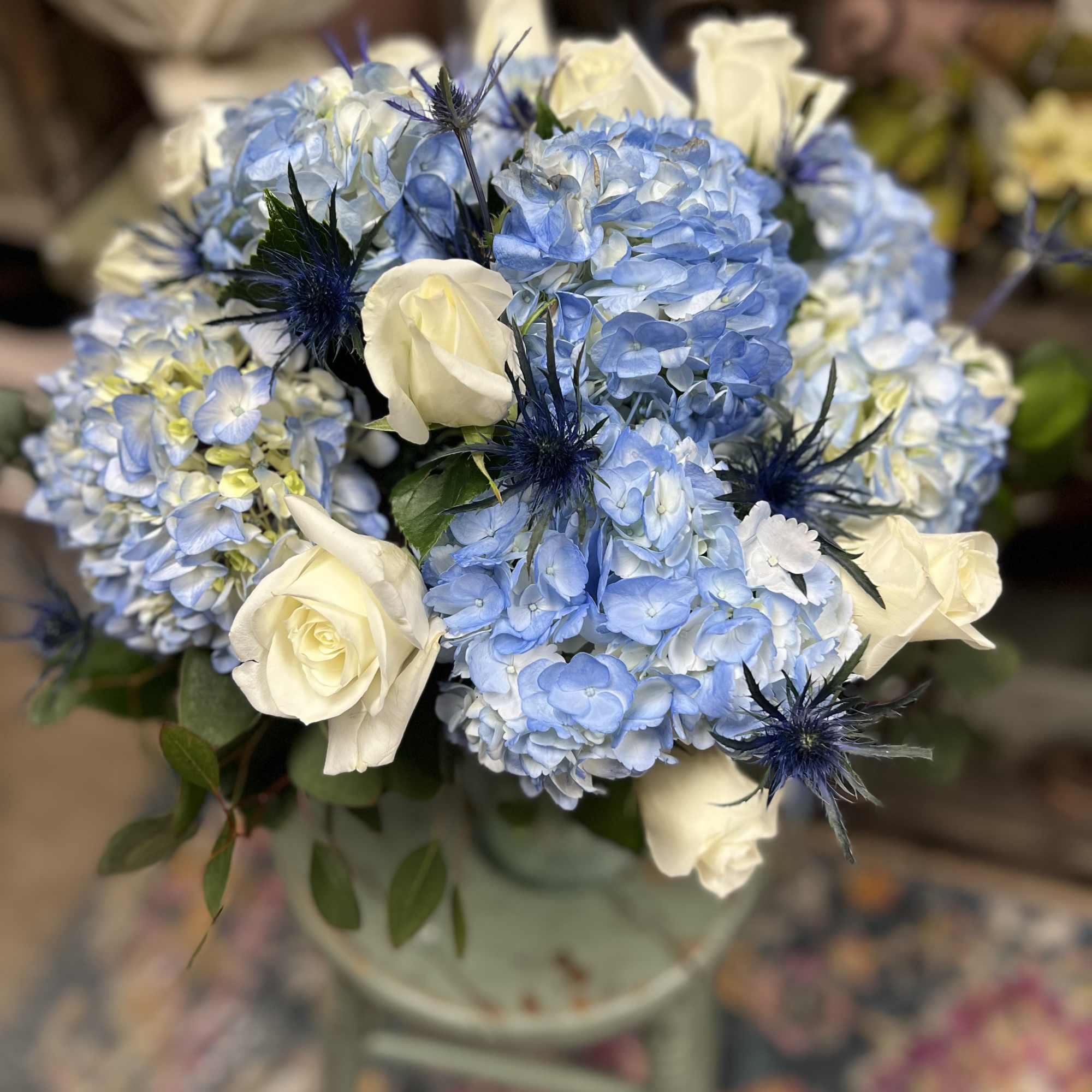 A beautifully arranged vase filled with Blue Hydrangeas and mixed greens (vase