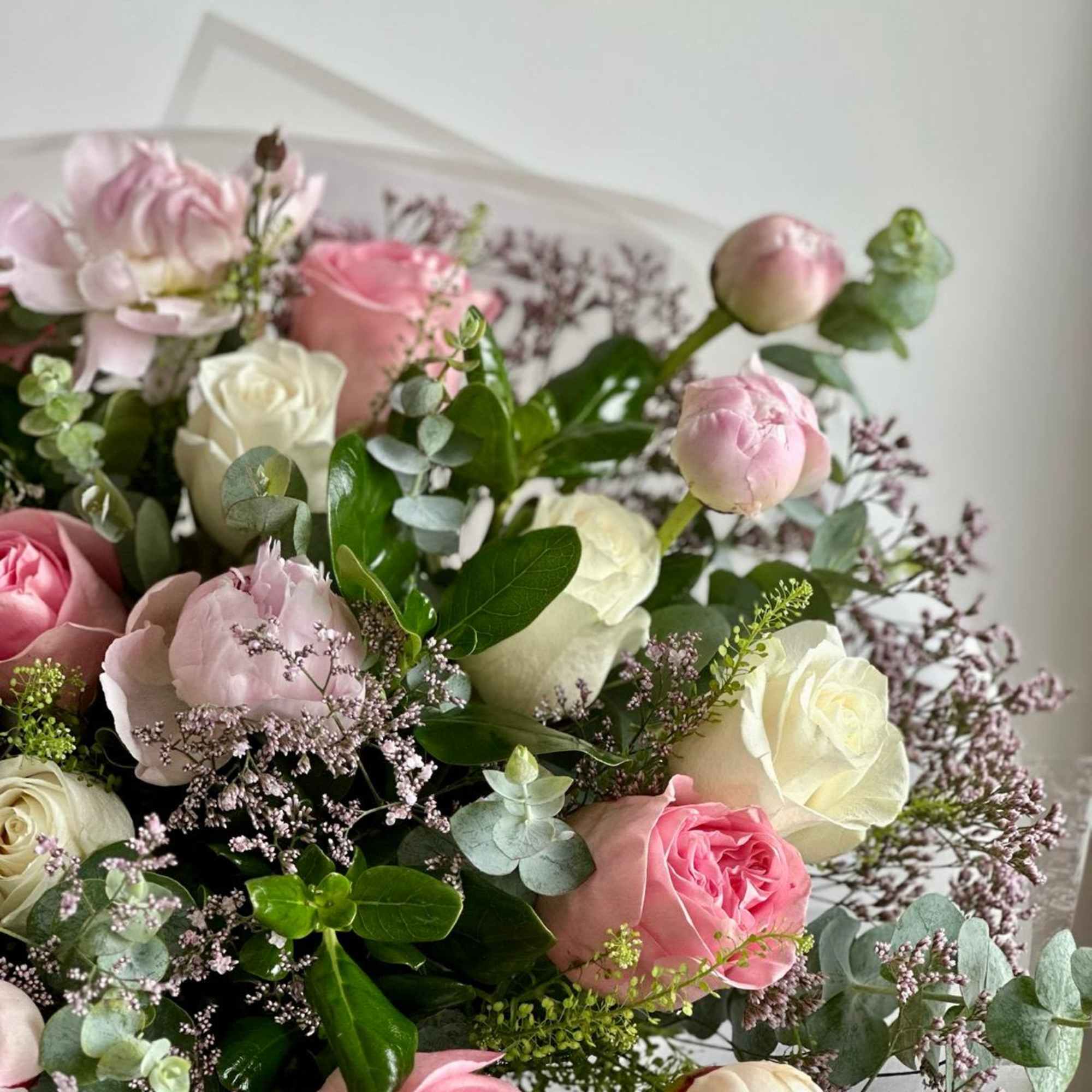 A round bouquet of white and pink flowers with lush greenery, wrapped