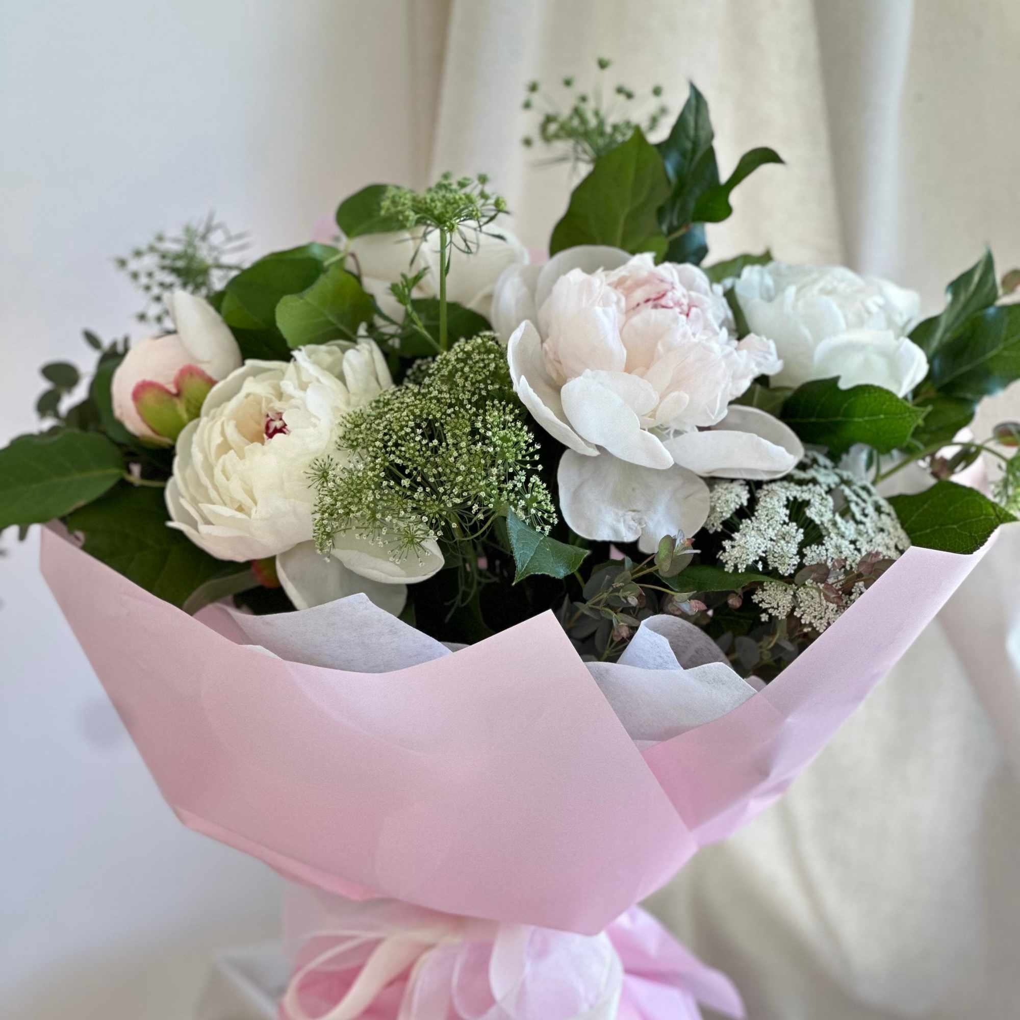 A round bouquet of lt. pink peonies with plenty of greenery and