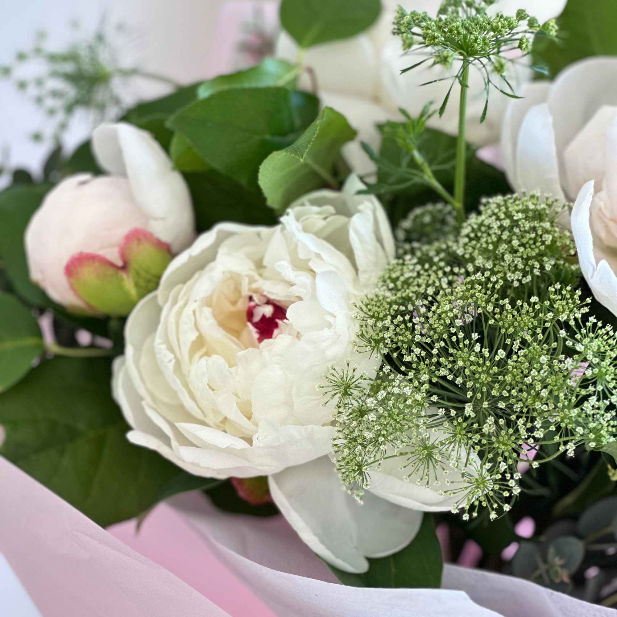 A round bouquet of lt. pink peonies with plenty of greenery and