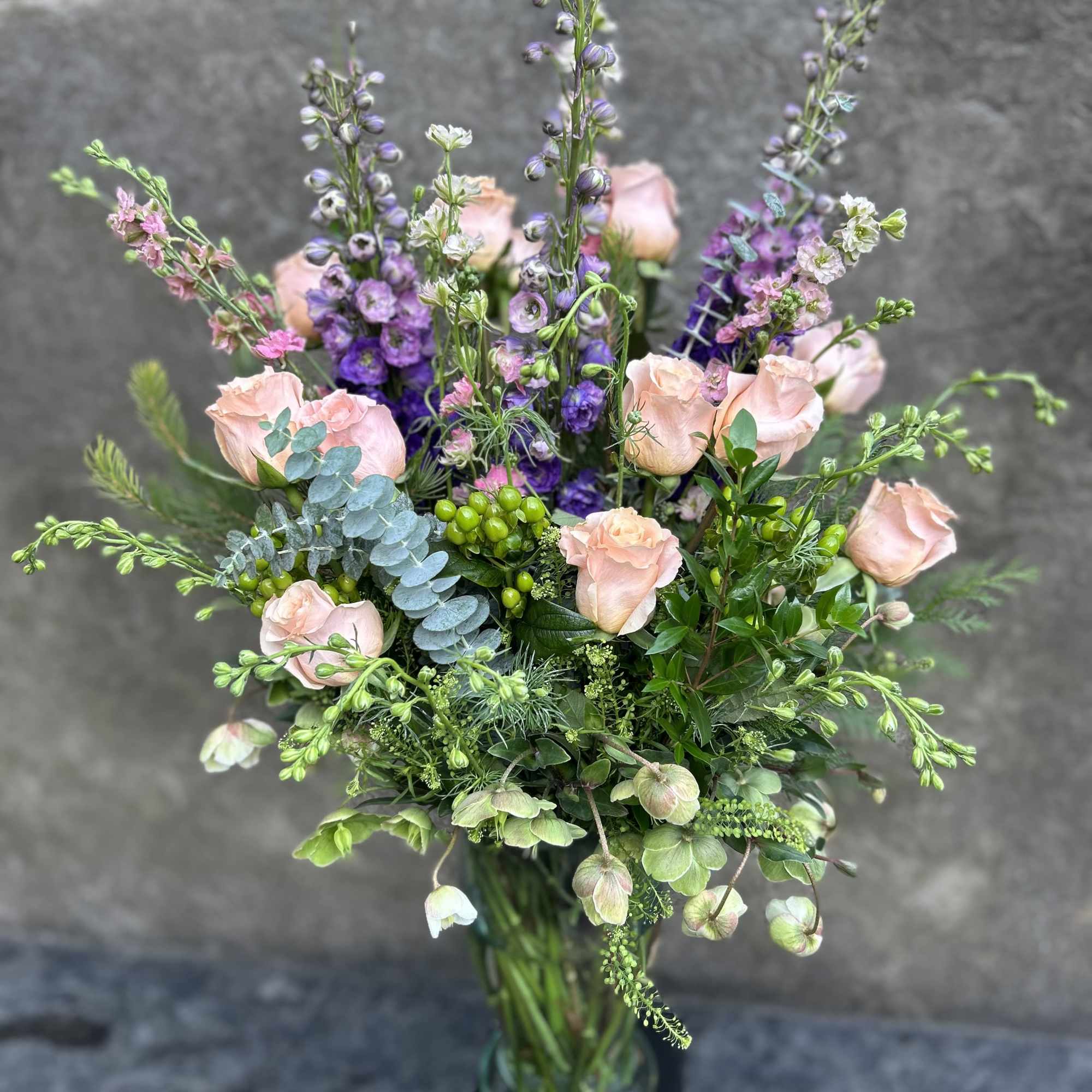 Peach roses, lavender delphinium, pink Larkspur, hellebore, berry, eucalyptus, and other pretty