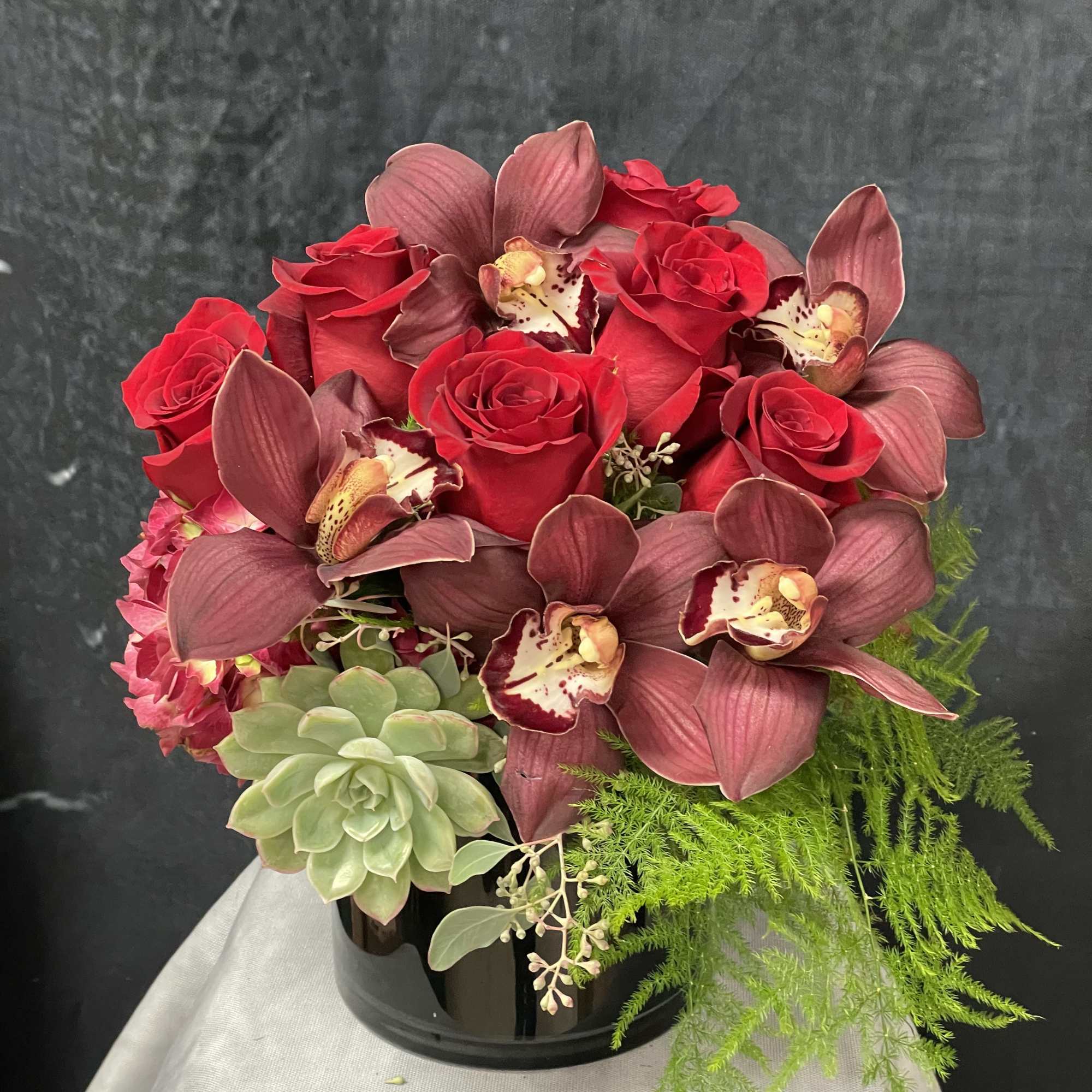 Natural red hydrangeas, red roses, burgundy cymbidiums, succulent and greenery in a
