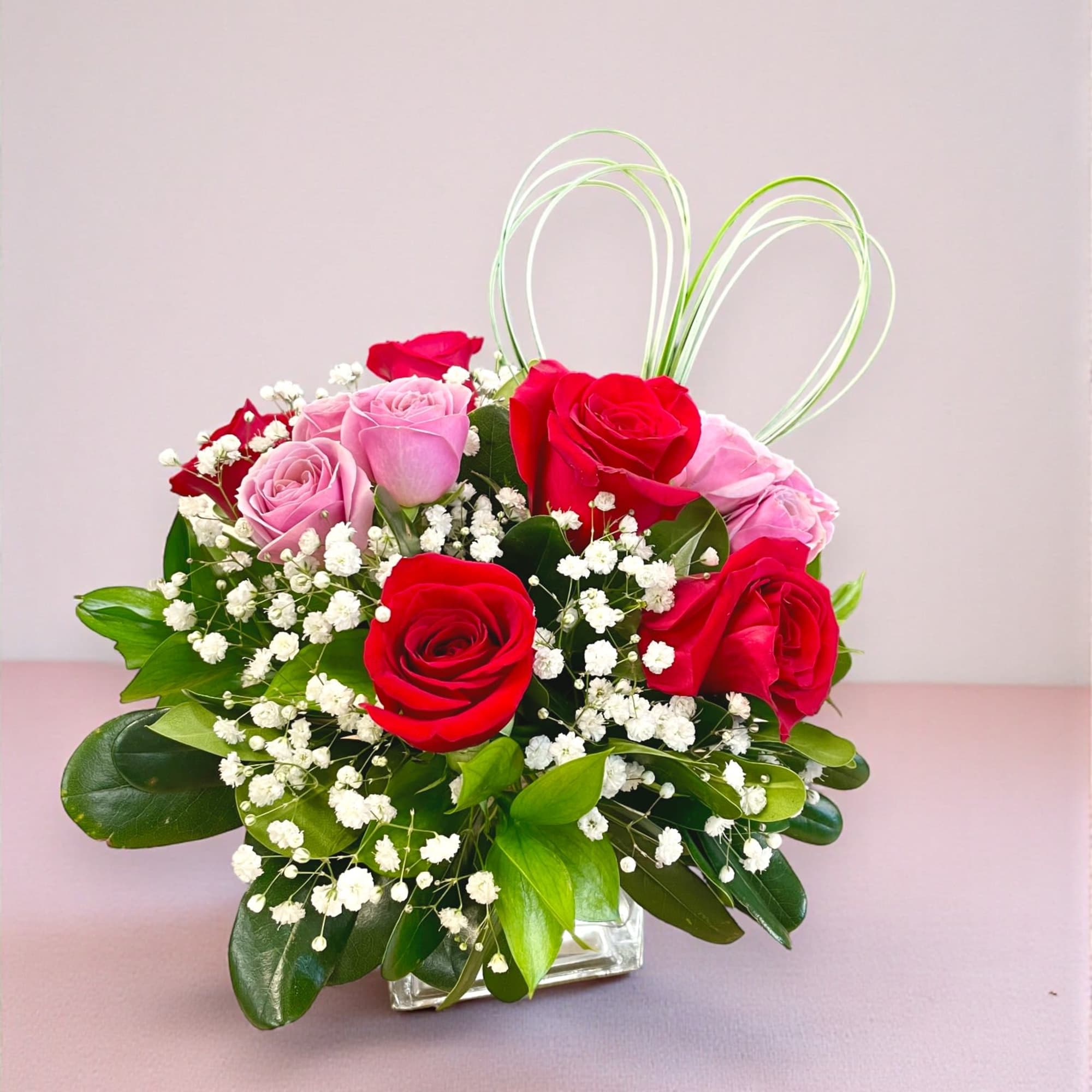 This Valentine's Day arrangement showcases six red roses and purple spray roses