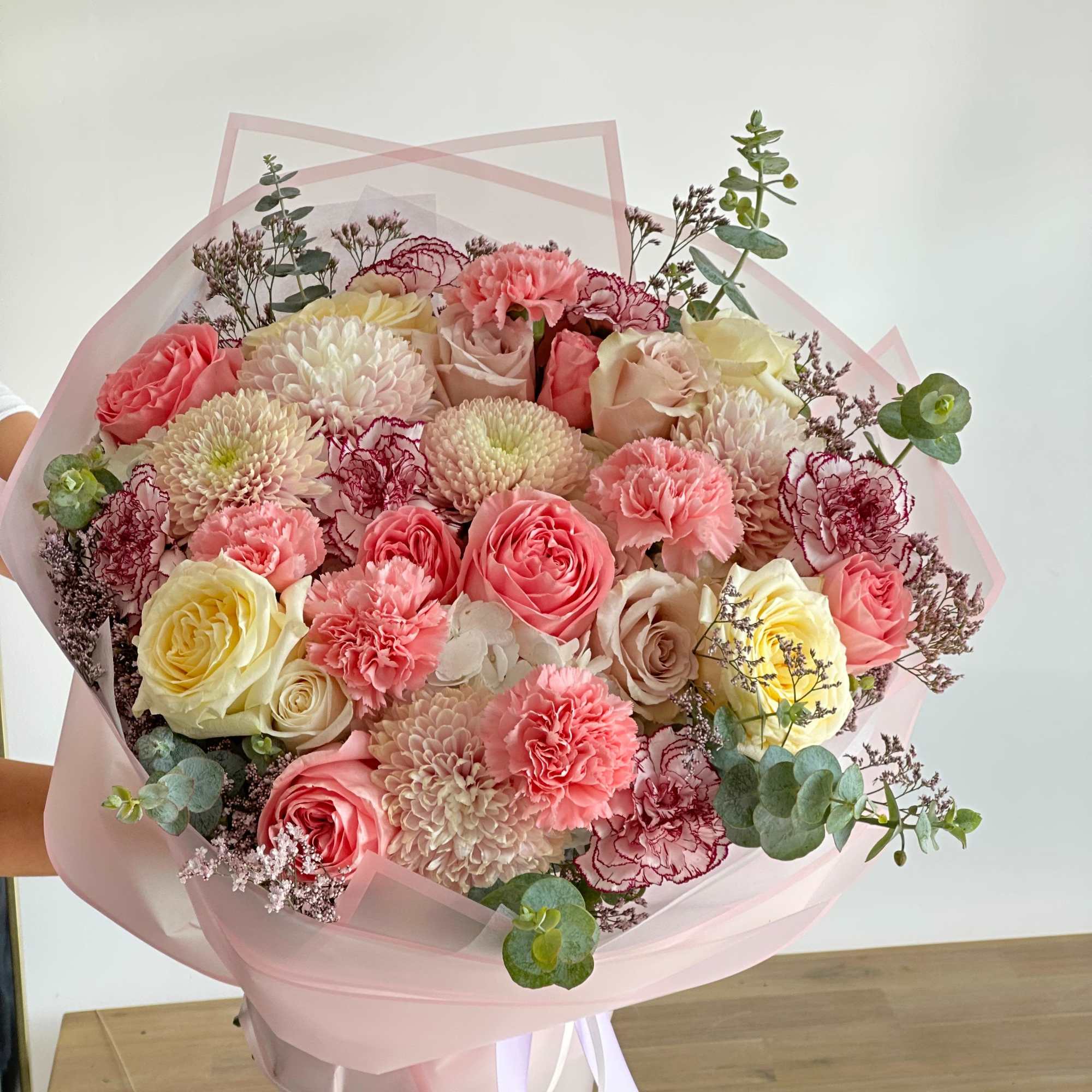 A round bouquet with white and pink flowers, wrapped in soft pink