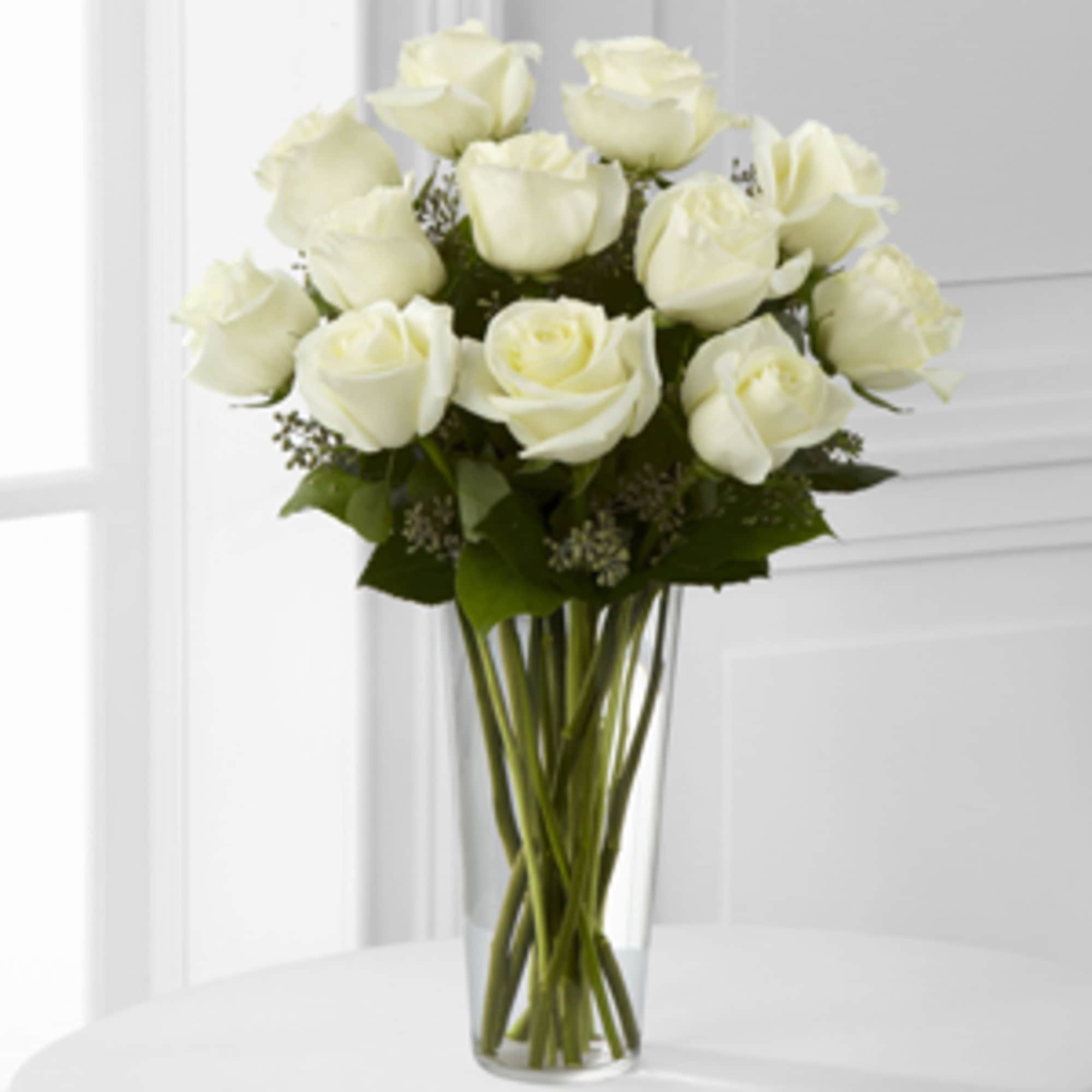 White roses are arranged in a sparkling glass vase, and accented with
