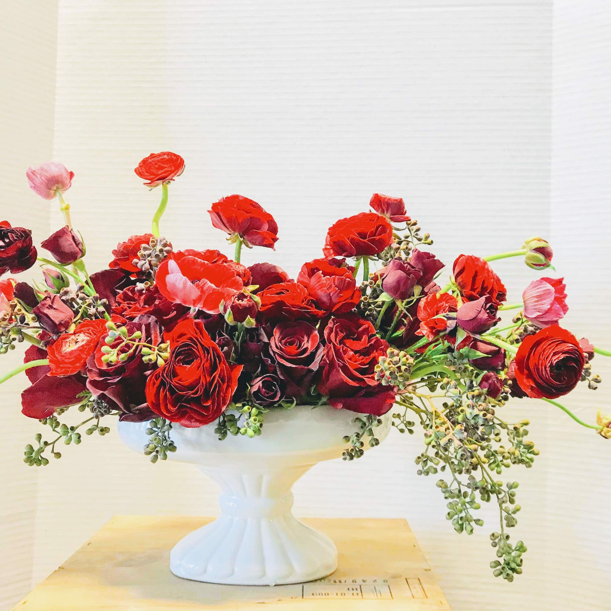 Oblong pedestal bowl filled and overflowing with red roses and ranunculas