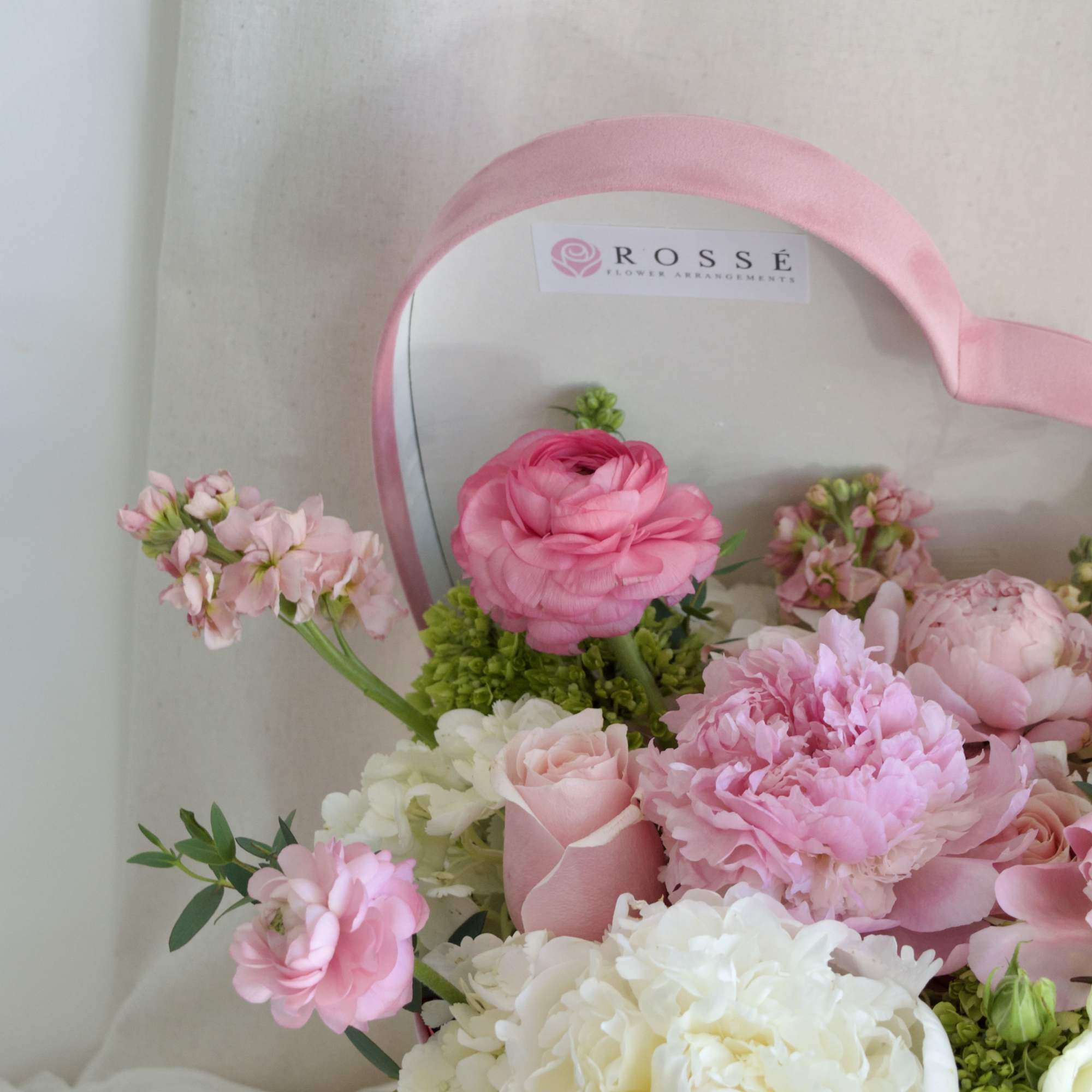 A heart-shaped pink velvet box filled with white, pink, and green flowers.