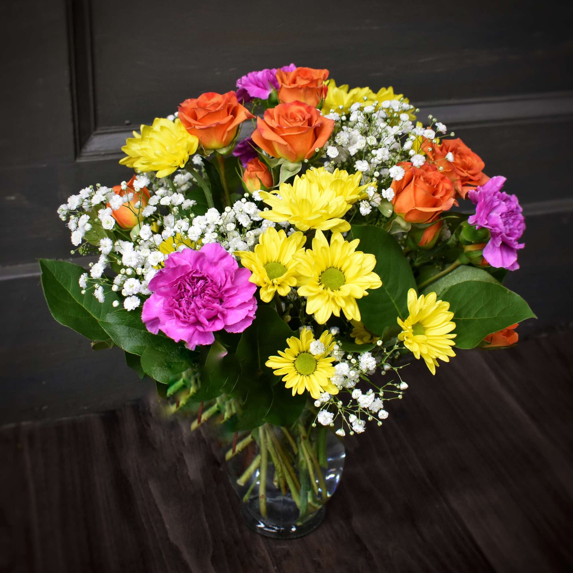 A clear glass vase filled with brightly colored daisies, carnations and spray