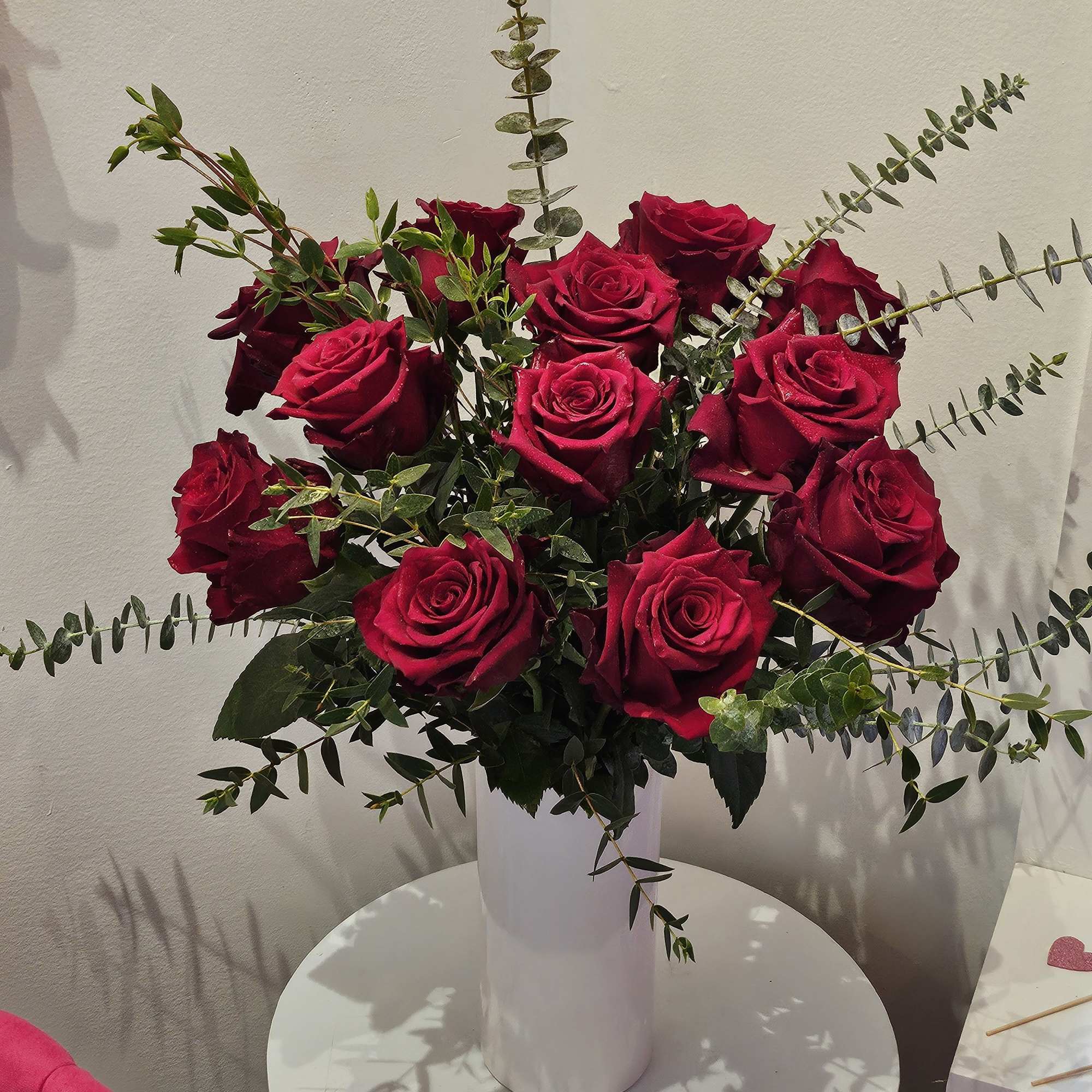Dozen red roses with greenery in a white ceramic vase