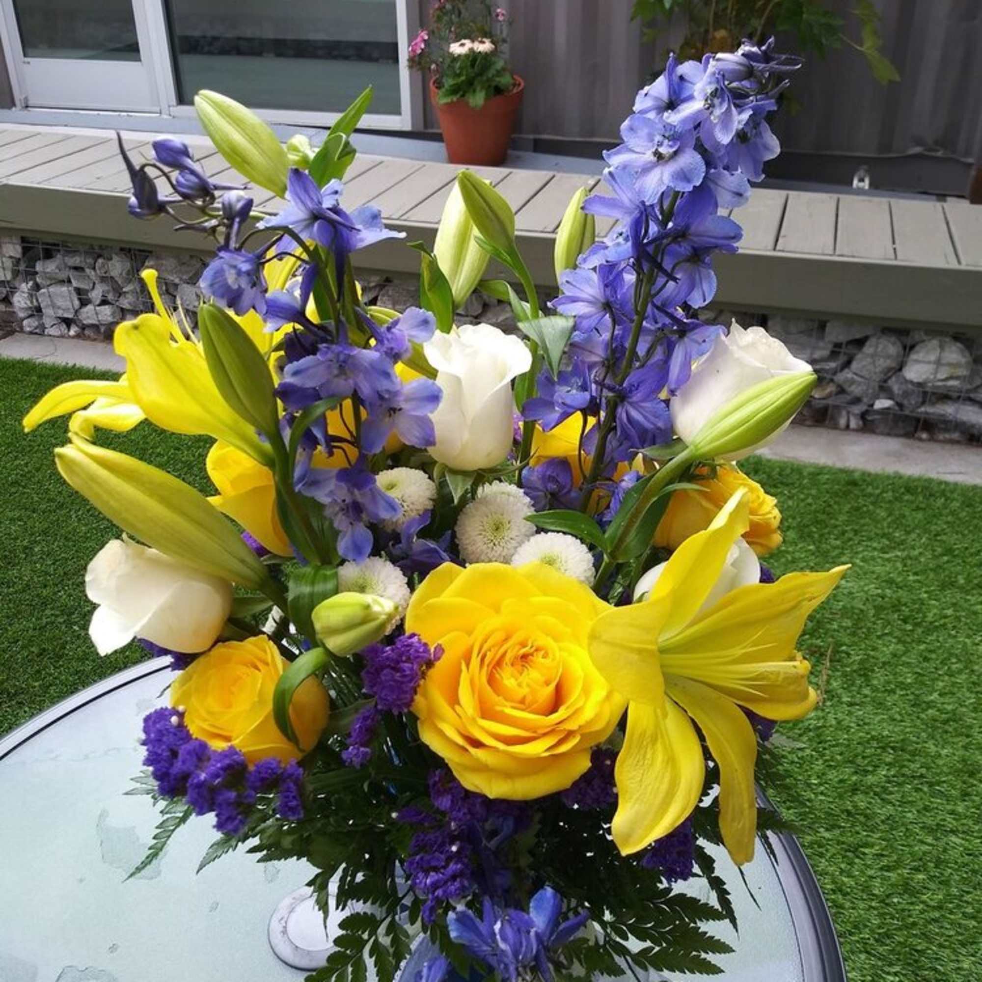 An arrangement of yellow roses, delphinium, white lilies, monte casino, greenery and