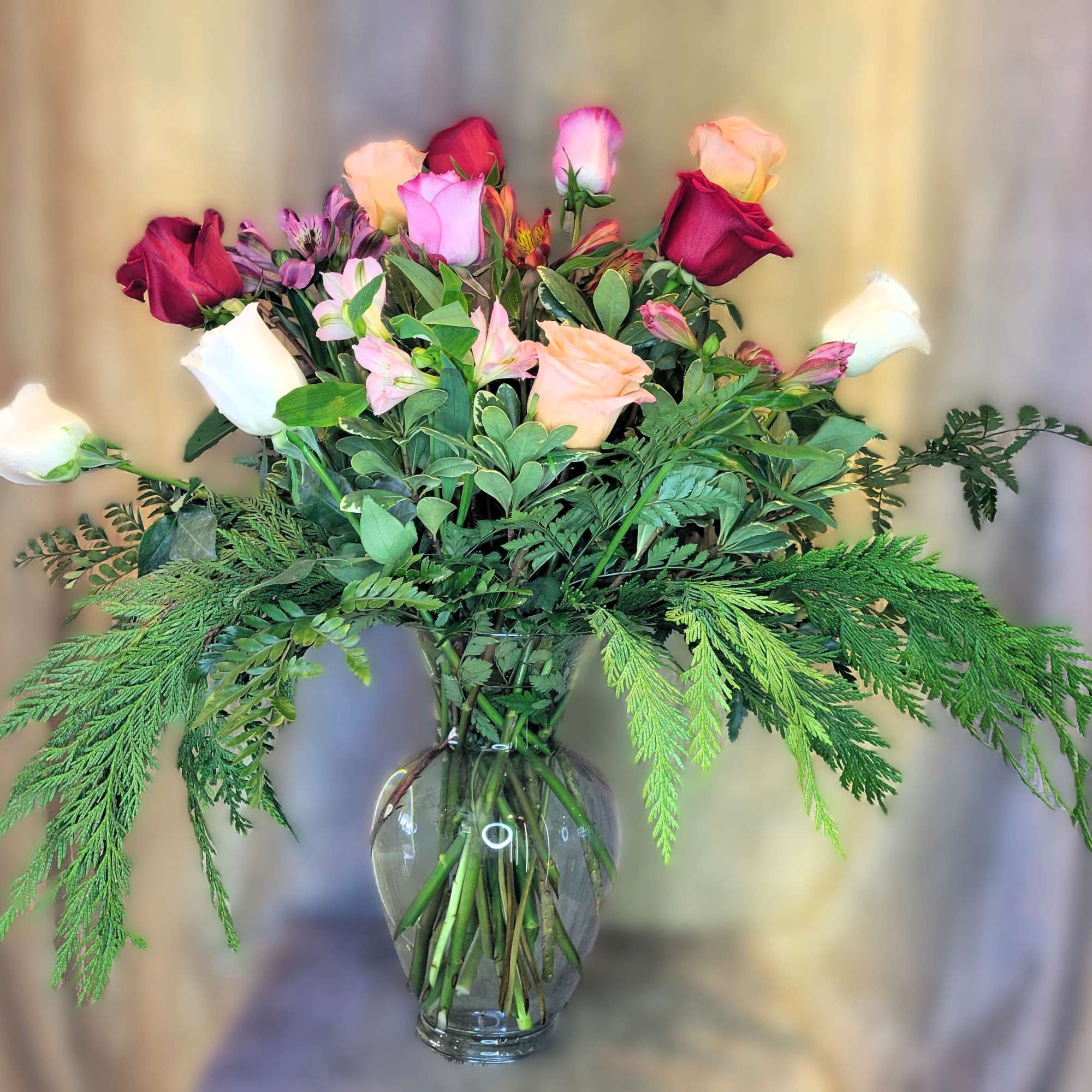 Premium one dozen multi-colored roses arranged beautifully in a clear glass vase.