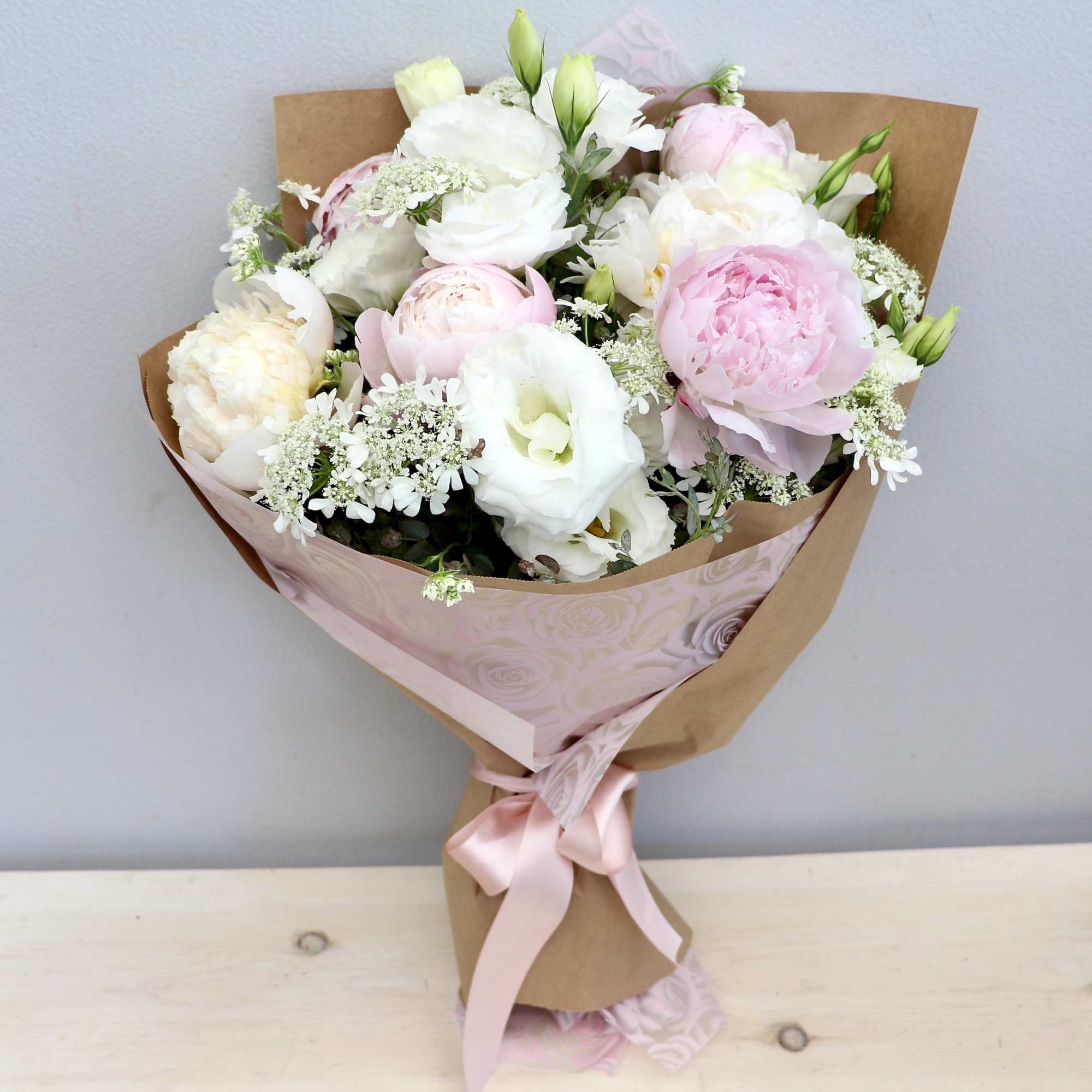This wrapped bouquet is with seasonal peonies and lisanthus and seasonal greens.