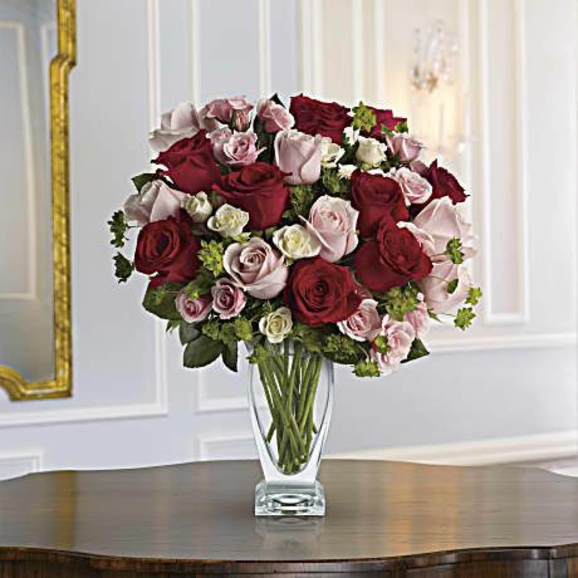 The lush bouquet includes red roses, pink roses, white spray roses and