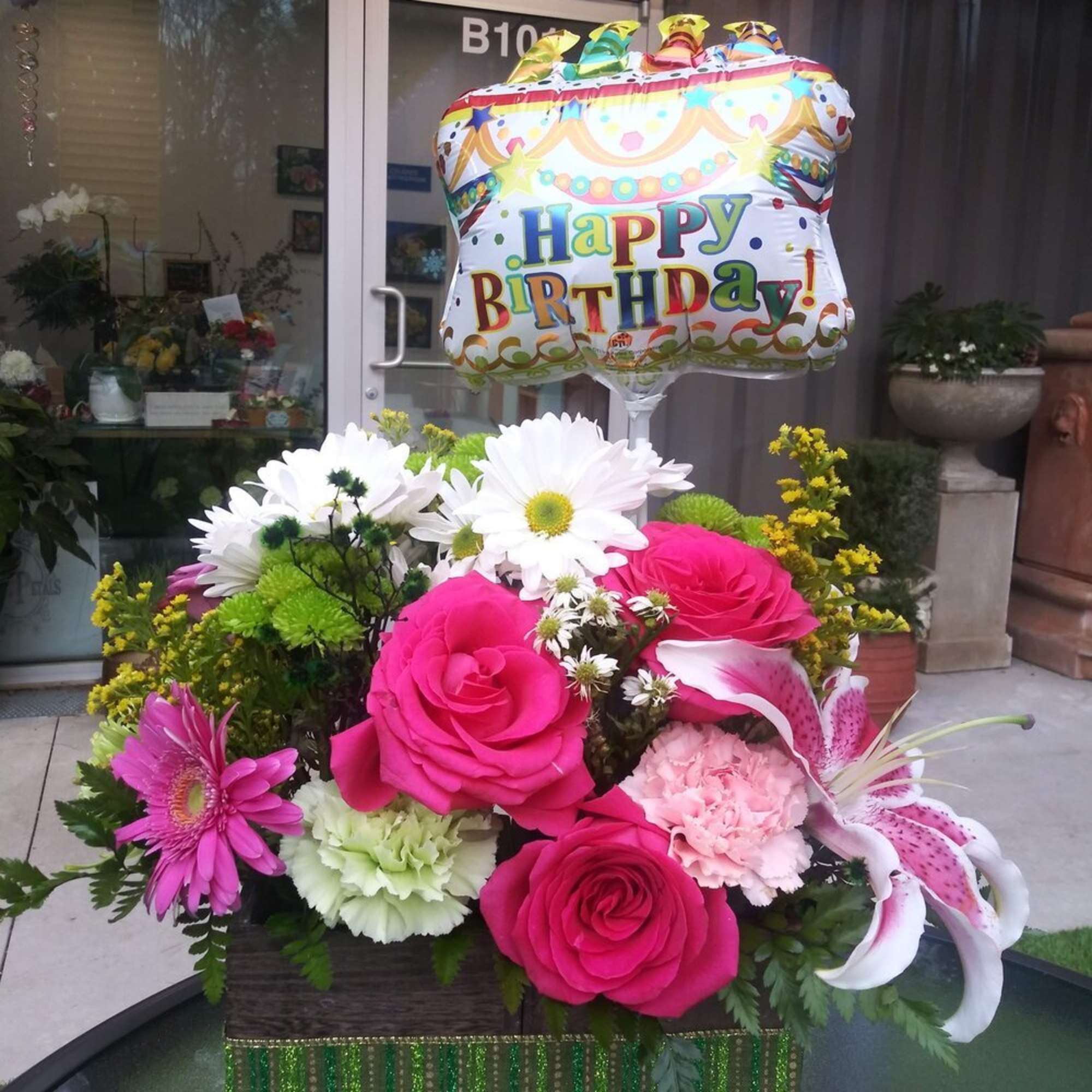 A wooden planter of hot pink roses, daisy mums, pom-poms, carnations, lilies