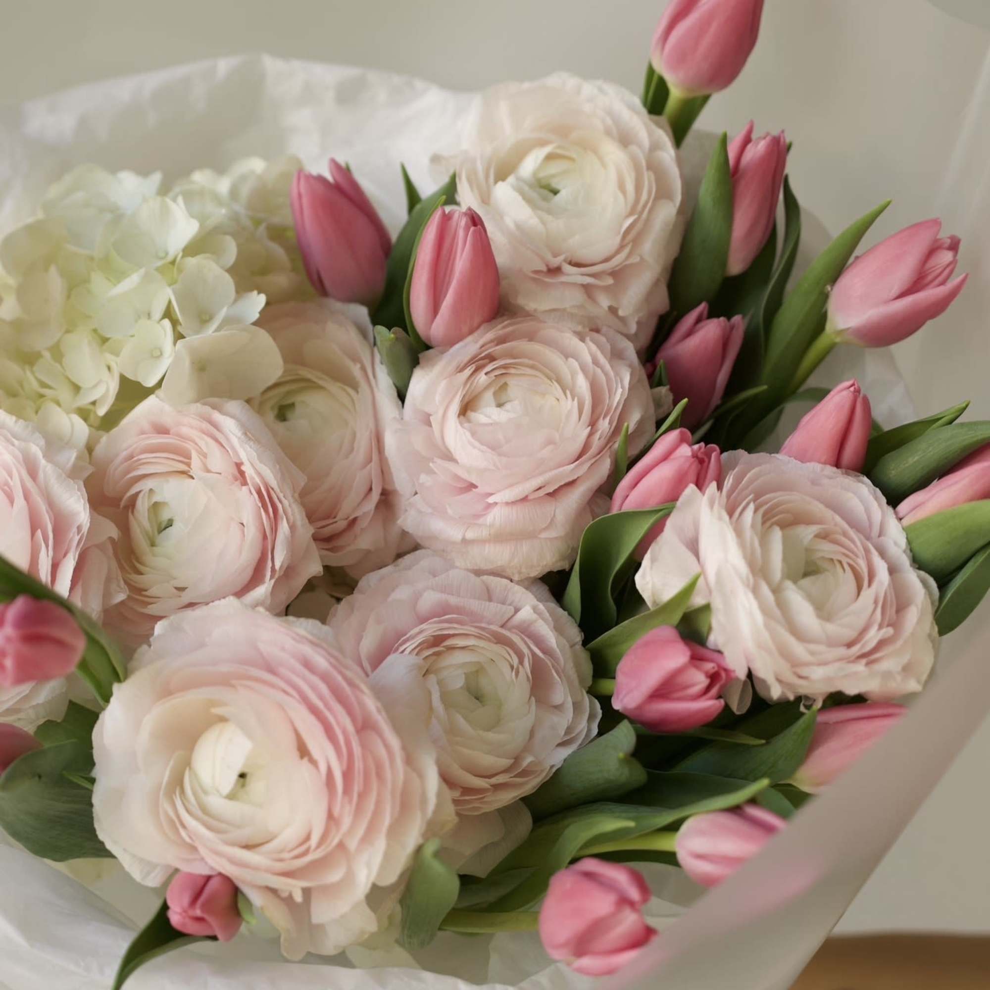 A delicate composition of blush ranunculus and soft pink tulips, designed to