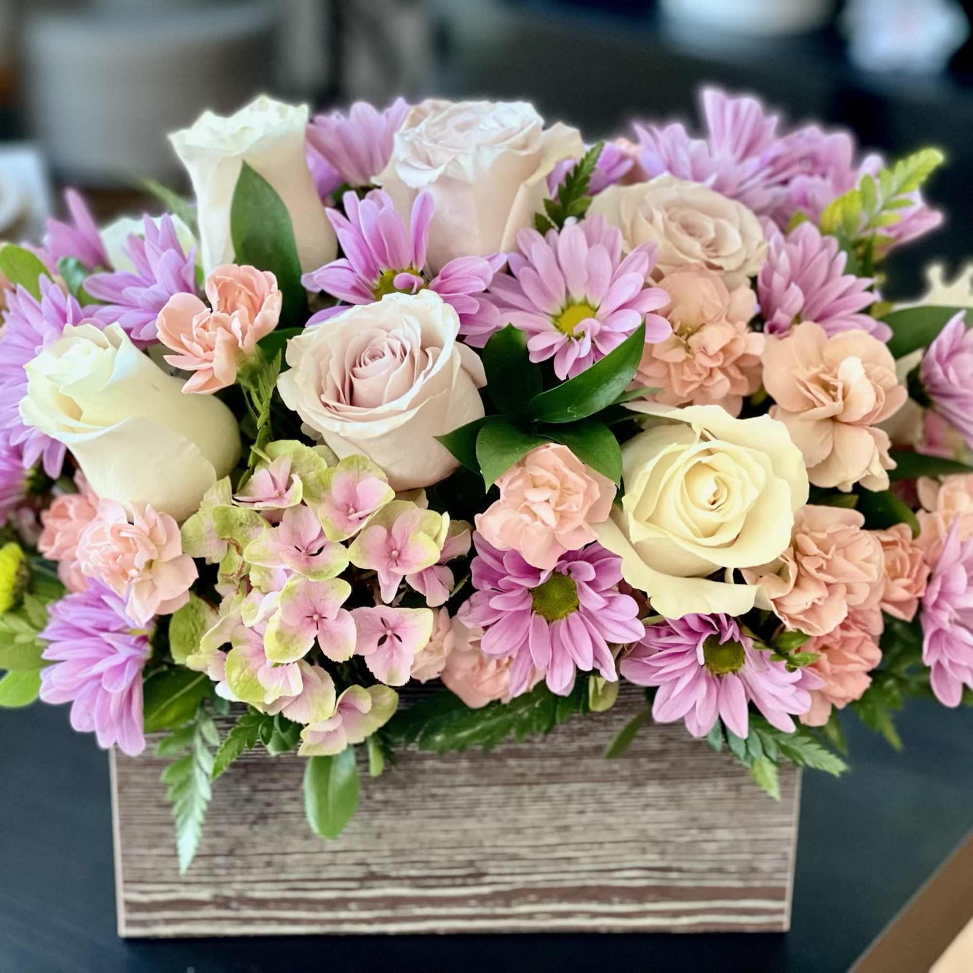 Nestled in a rustic wooden box, delicate lavender chrysanthemums, pristine white roses