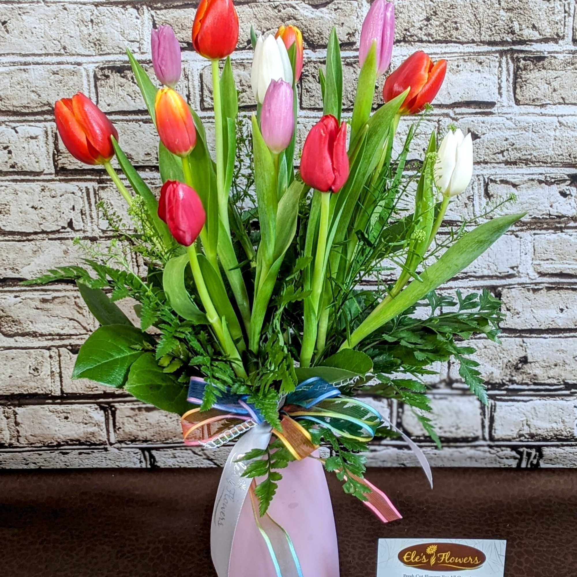 An arrangement of a dozen mixed-color tulips, artfully paired with fresh greenery