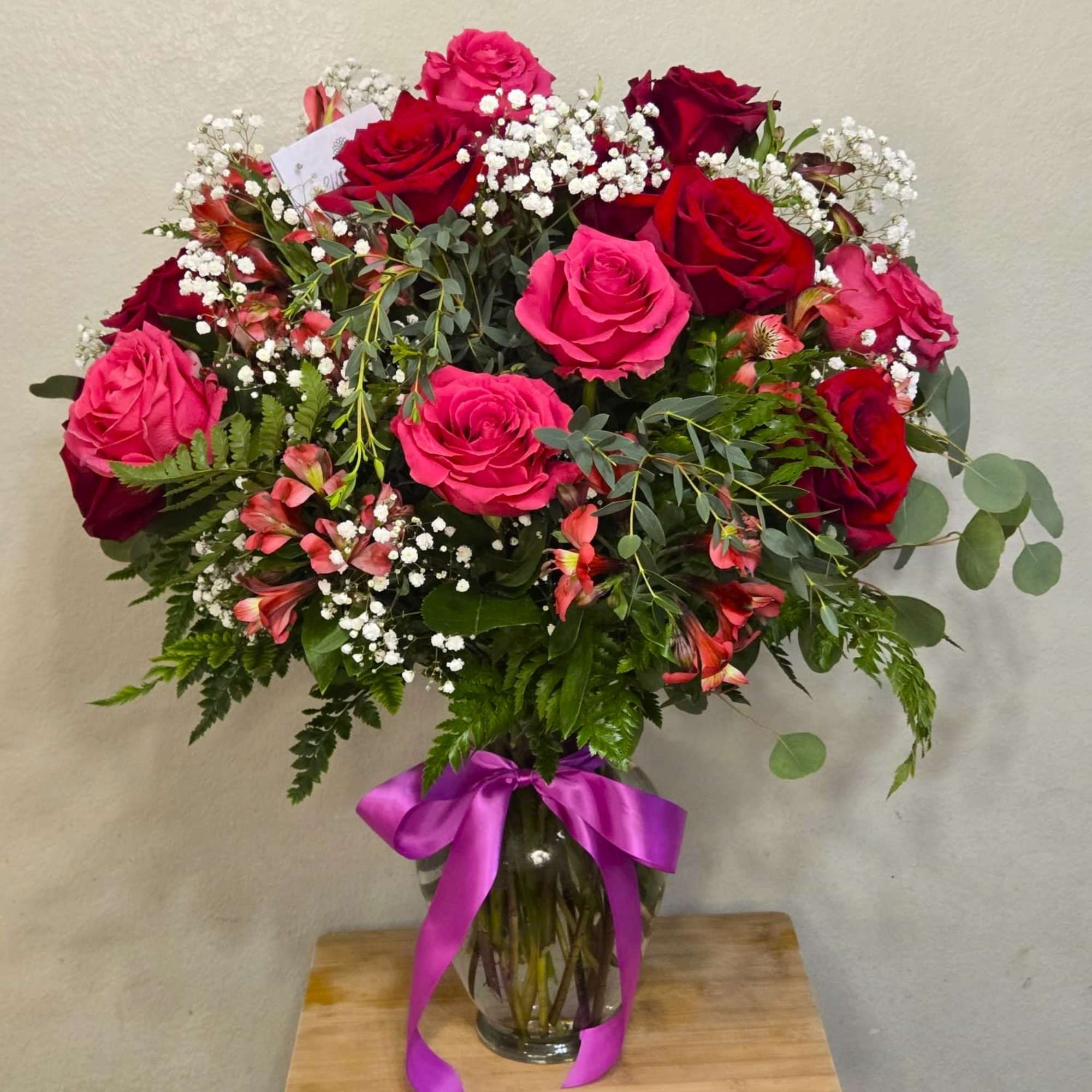 Clear vase arrangement with 16 red and pink roses, green foliage, alstroemeria