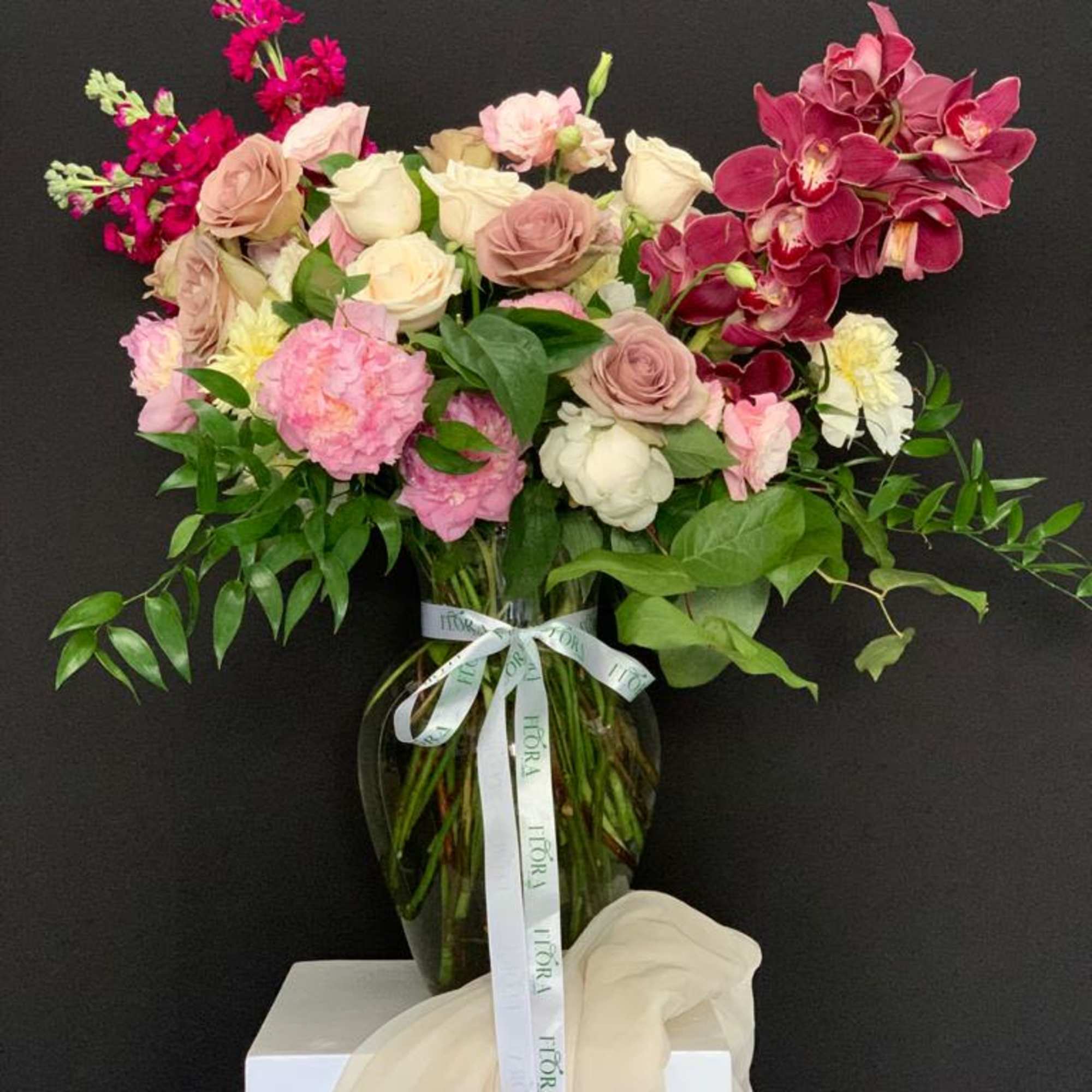 Stunning organic shape arrangement featuring beautiful roses, peonies, stock, and cymbidium orchids.