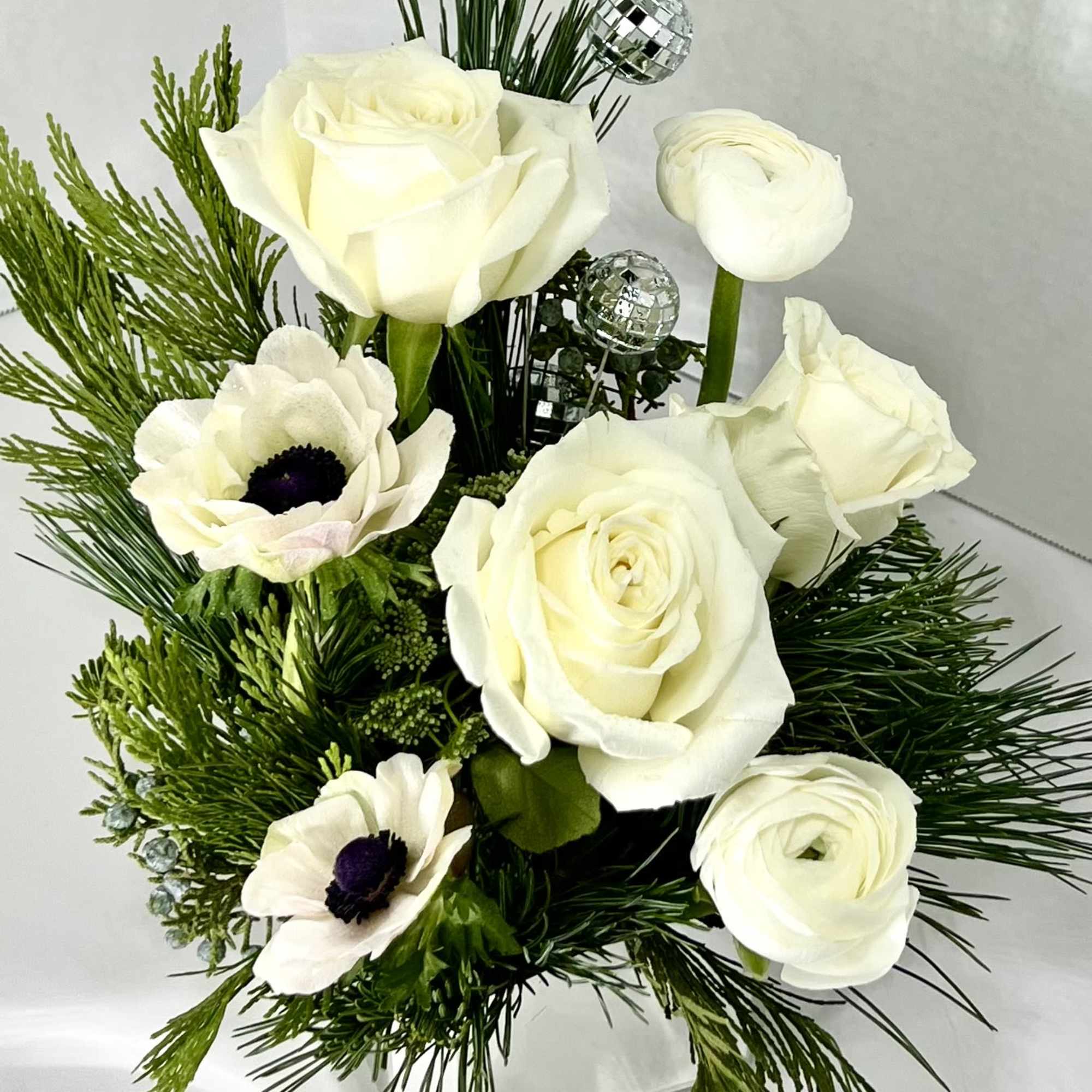 Stunning mix of white blossoms nestled into long lasting winter evergreens. 