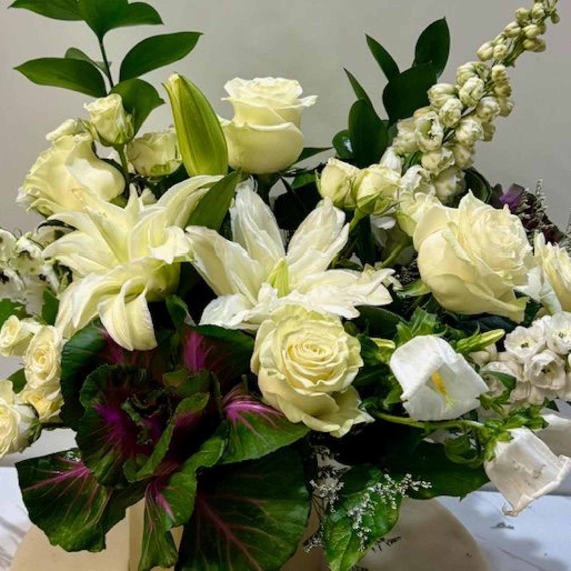 An elegant white and green arrangement featuring textured kale, white roses, delphinium