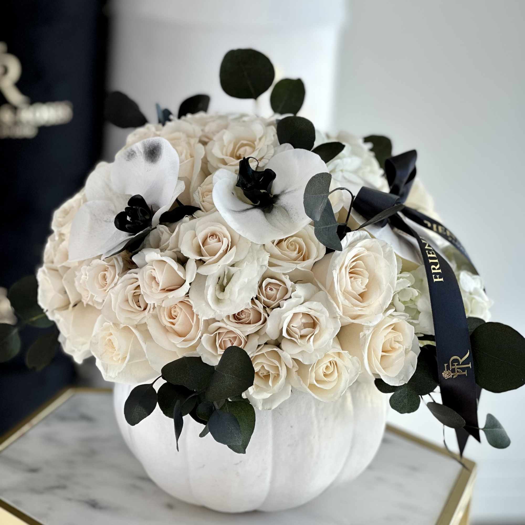 A chic floral arrangement in a white pumpkin, featuring white roses and