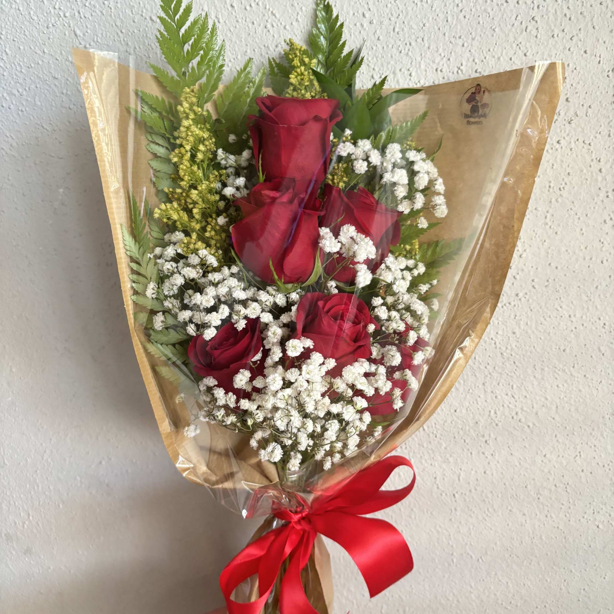 Six red roses with baby's breath and greenery, wrapped in paper and