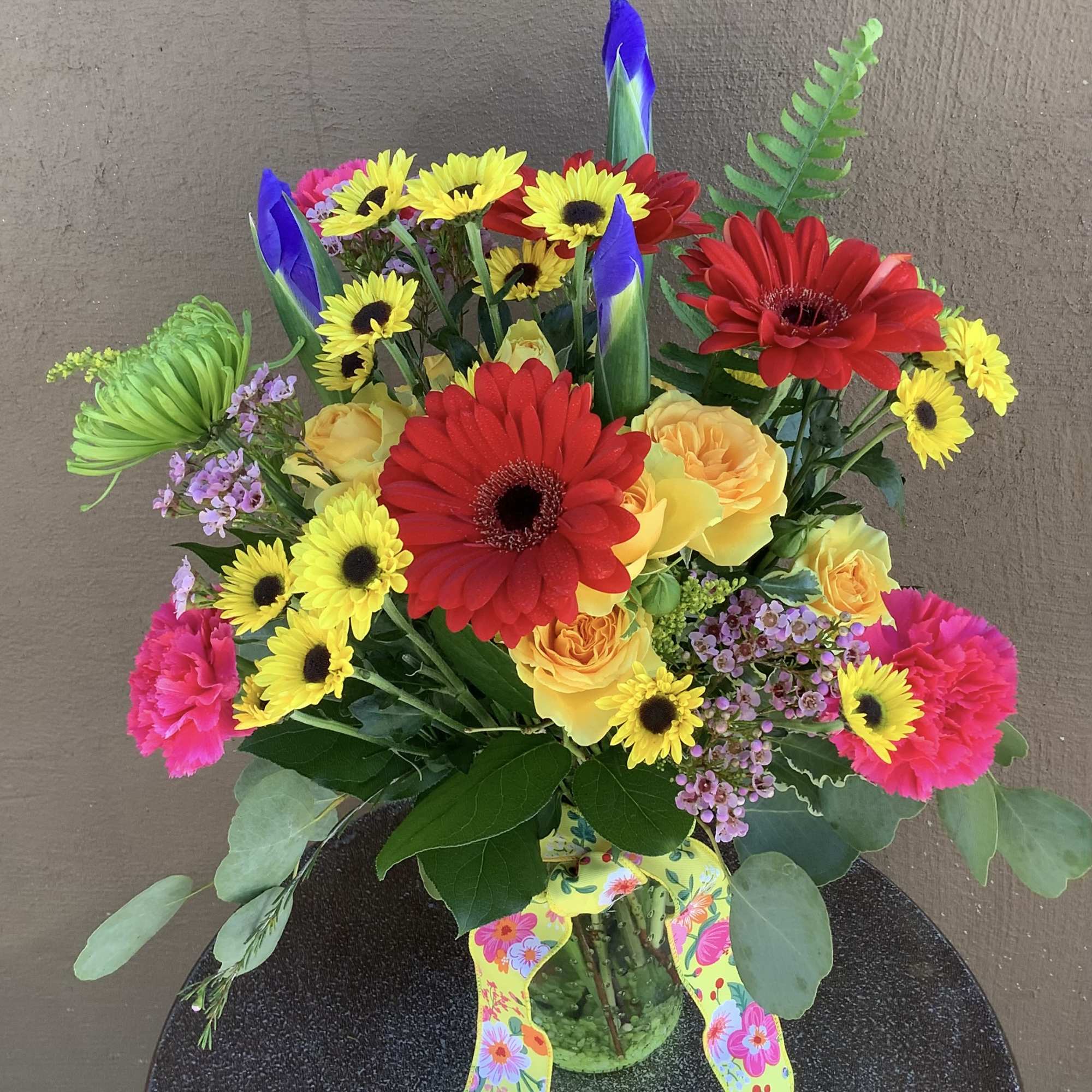 Vase of bright gerbera, fugi mums, iris, button mums, spray roses and