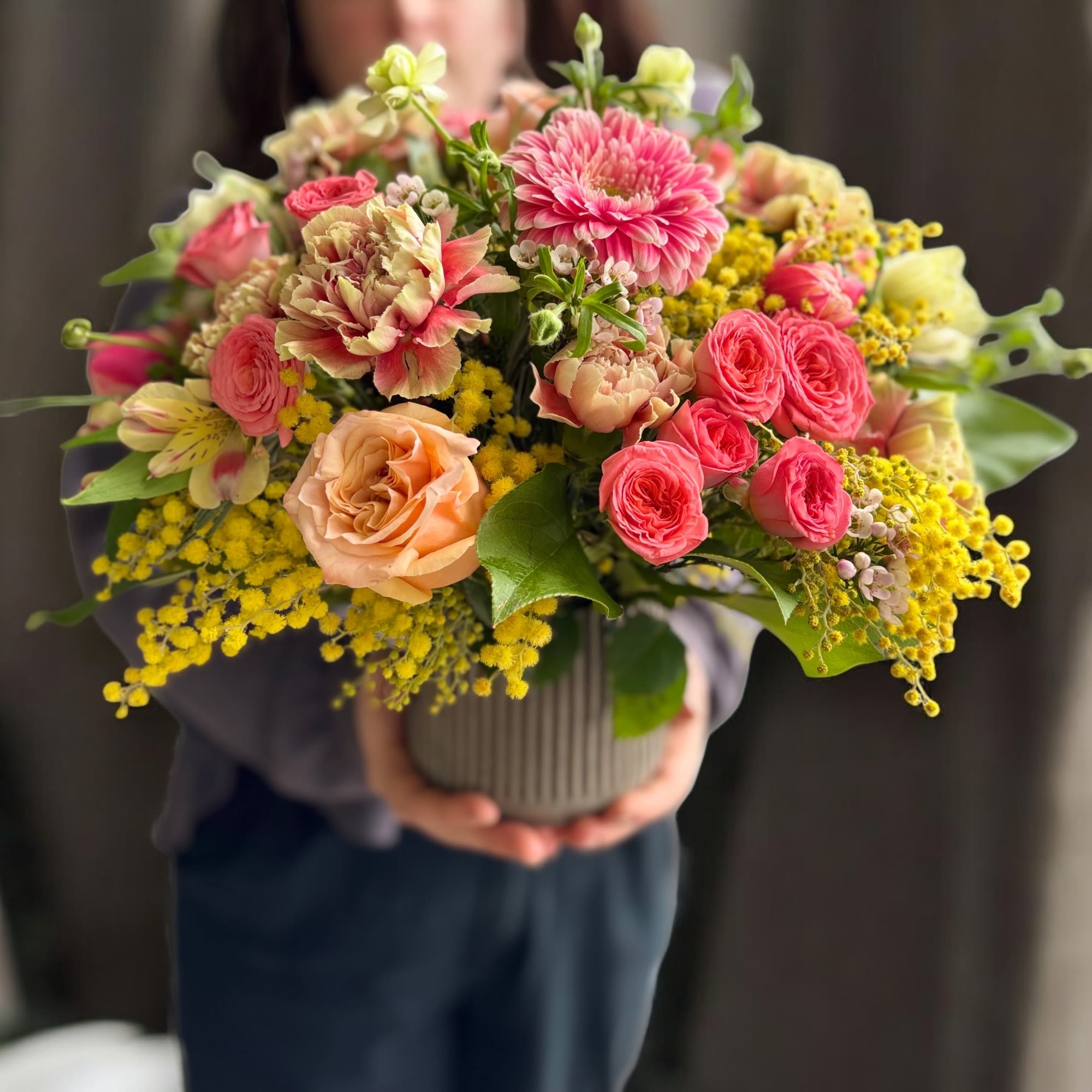 A seasonal arrangement of fragrant mimosa, coral spray roses and peach roses.