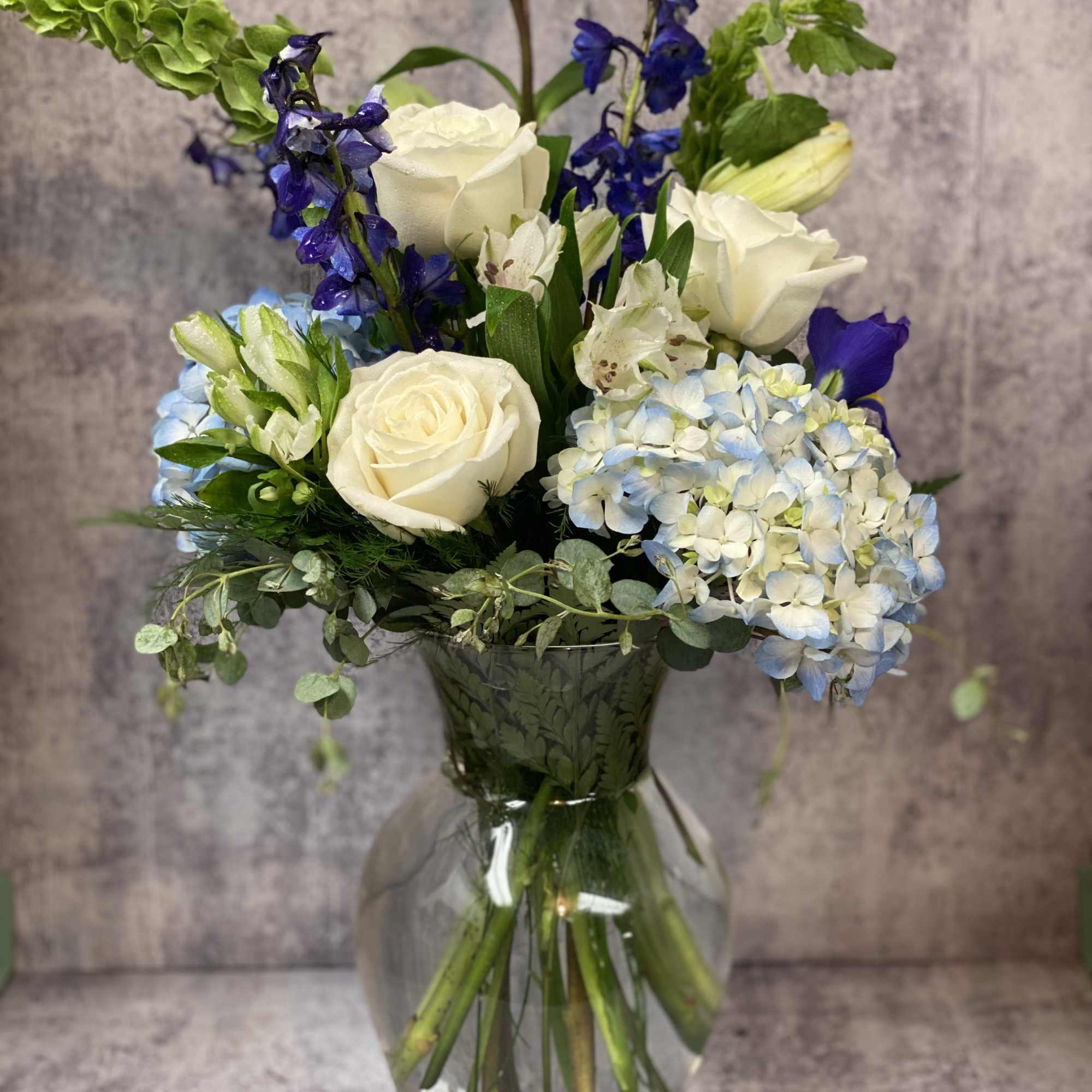 This arrangement contains delphinium, bells of ireland, asiatic lilies, hydrangea, blue iris