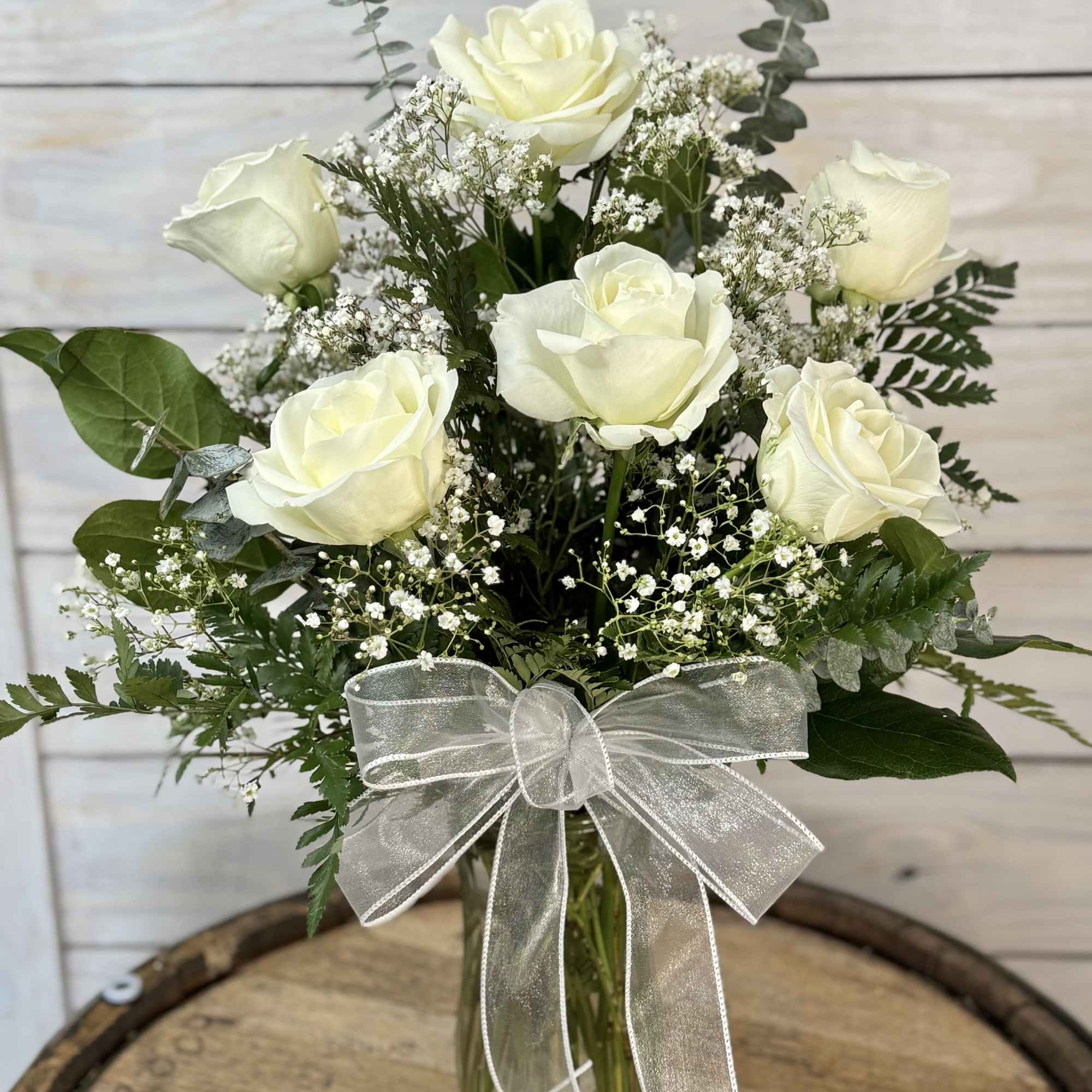 6 White roses with filler flowers arranged in vase. The white rose